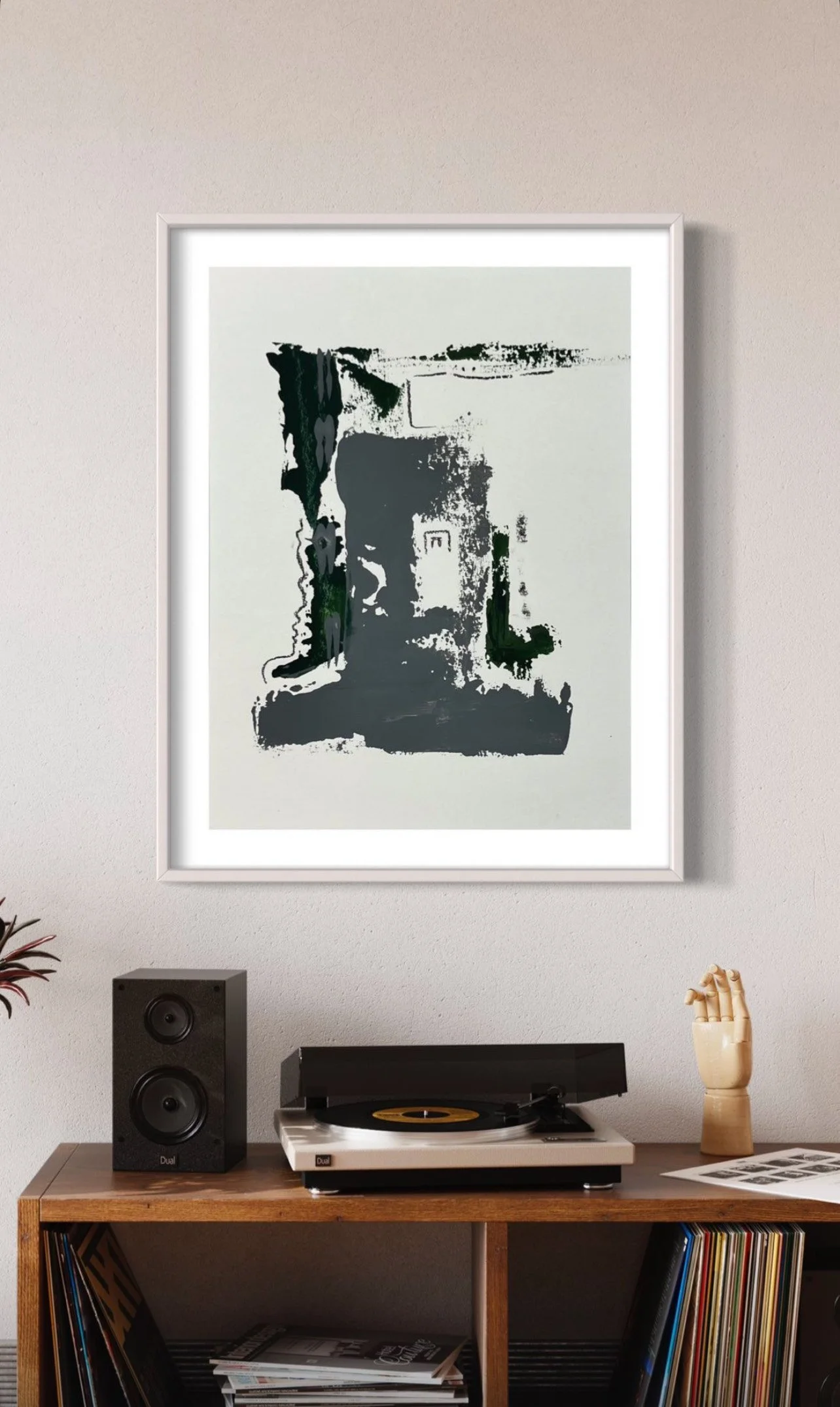 Black and white abstract art print hanging on a light-colored wall above a vintage wooden console table with a turntable, speakers, and a wooden hand sculpture.