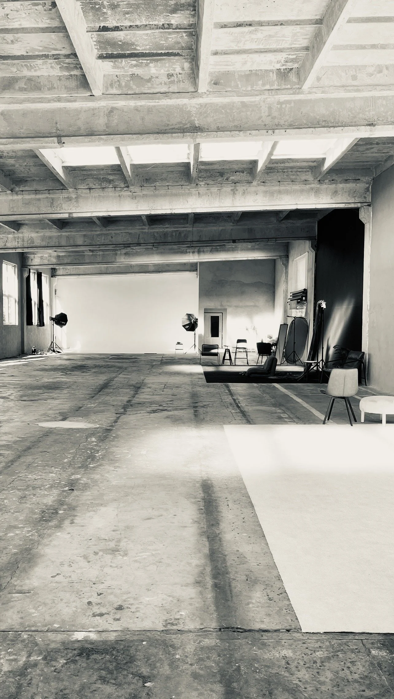 Empty photography studio with professional lighting equipment, chairs, and a backdrop, featuring a studio space with concrete floors and unfinished ceiling.