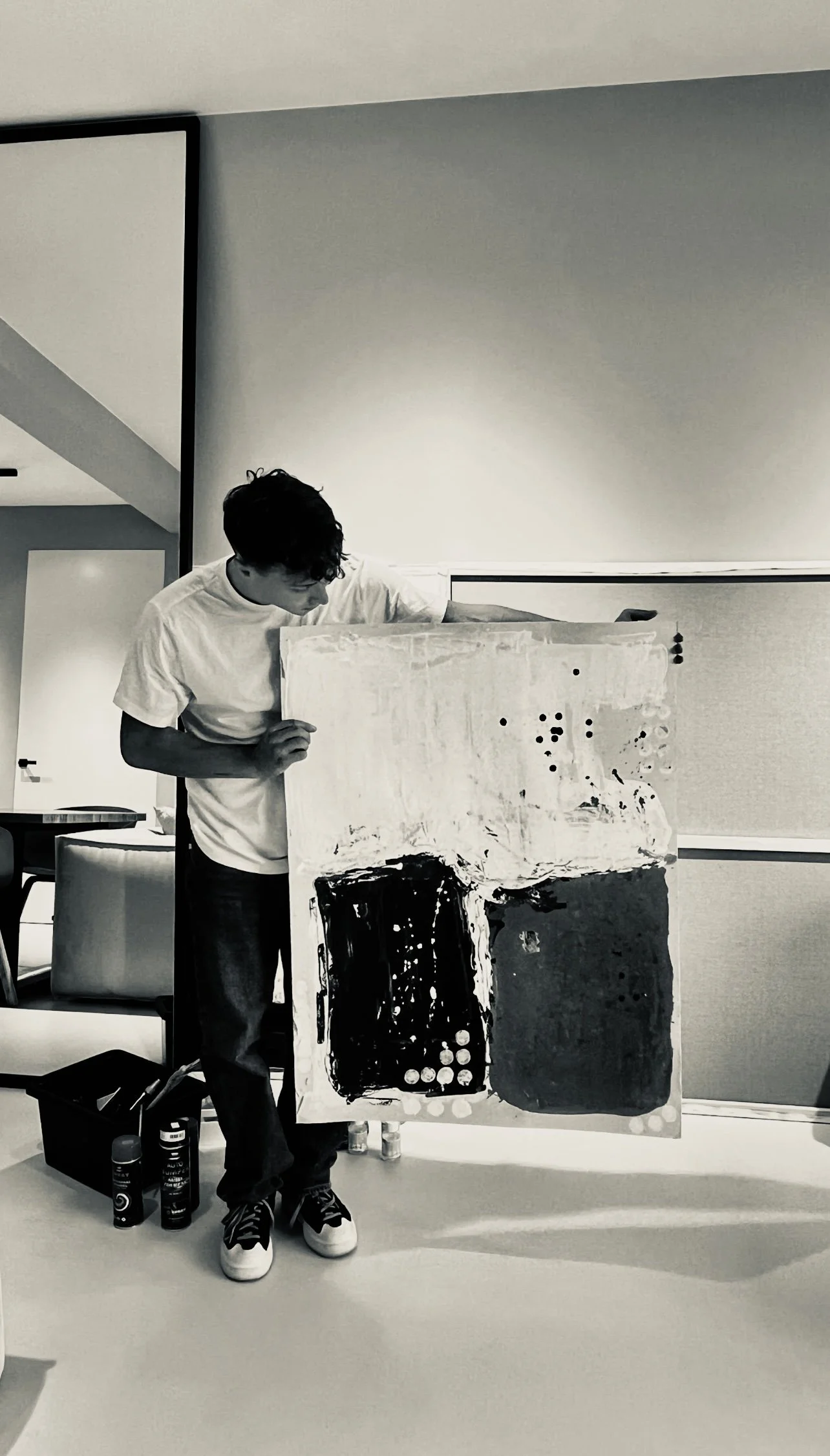 A person holding an abstract black and white painting in a modern room.