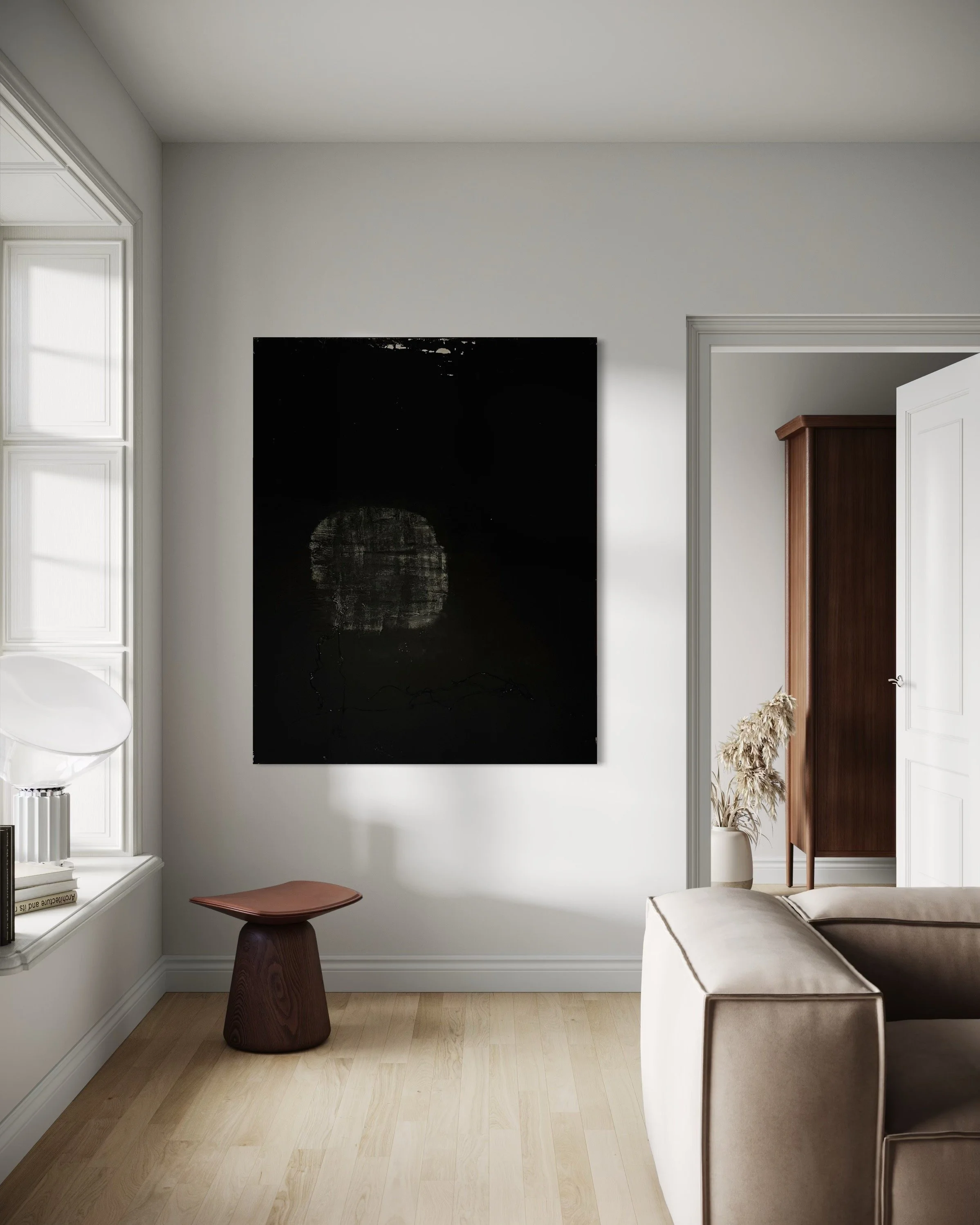 A living room corner with a black abstract art piece on a white wall, a beige sofa, a small wooden stool with a brown leather top, a window with white framing, a built-in window seat with books and a white lamp, and a doorway revealing a tall wooden 