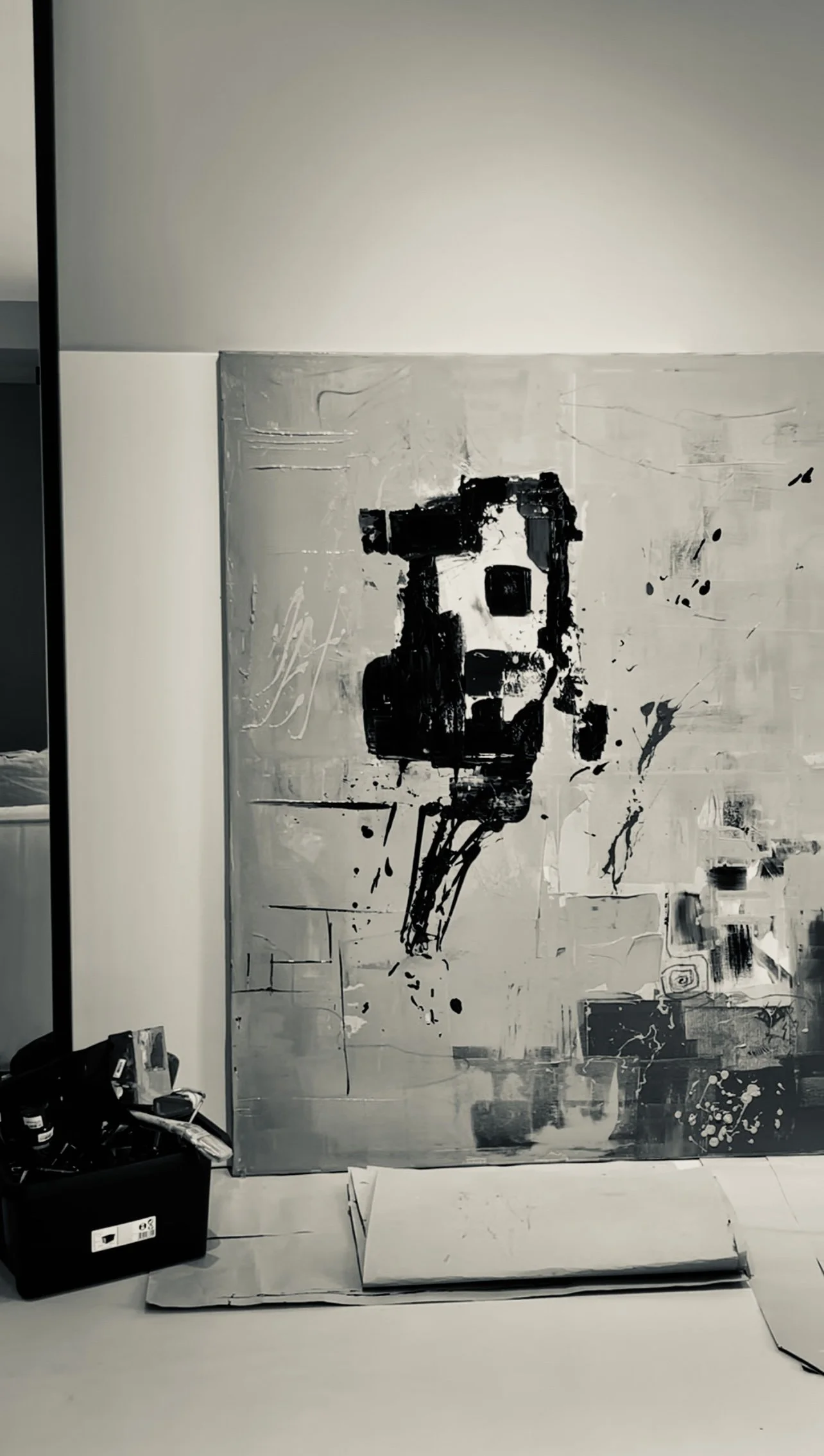 Black and white abstract painting of a robot or machine on a large canvas leaning against a wall.