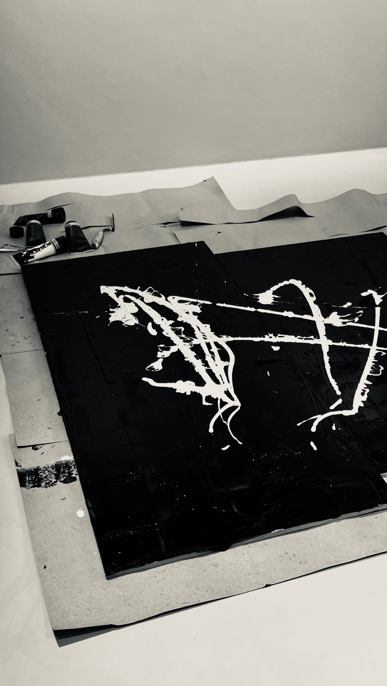 Black canvas with white abstract graffiti-style lines, laying on a concrete floor with art supplies nearby.
