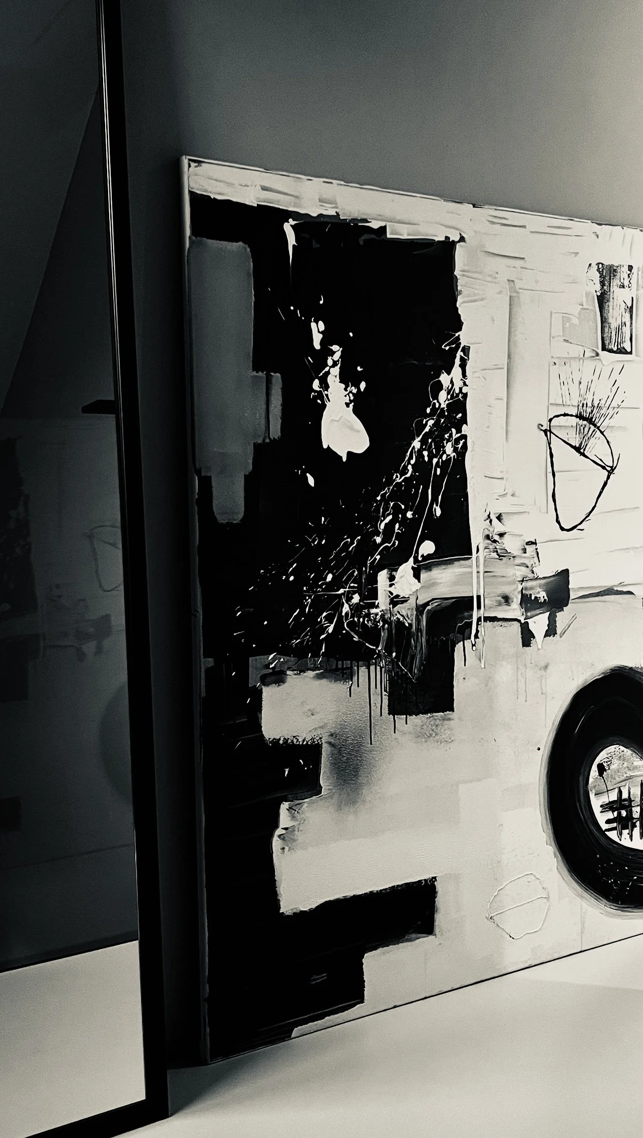 Abstract black and white painting with splashes and geometric shapes, partially leaning against a wall.
