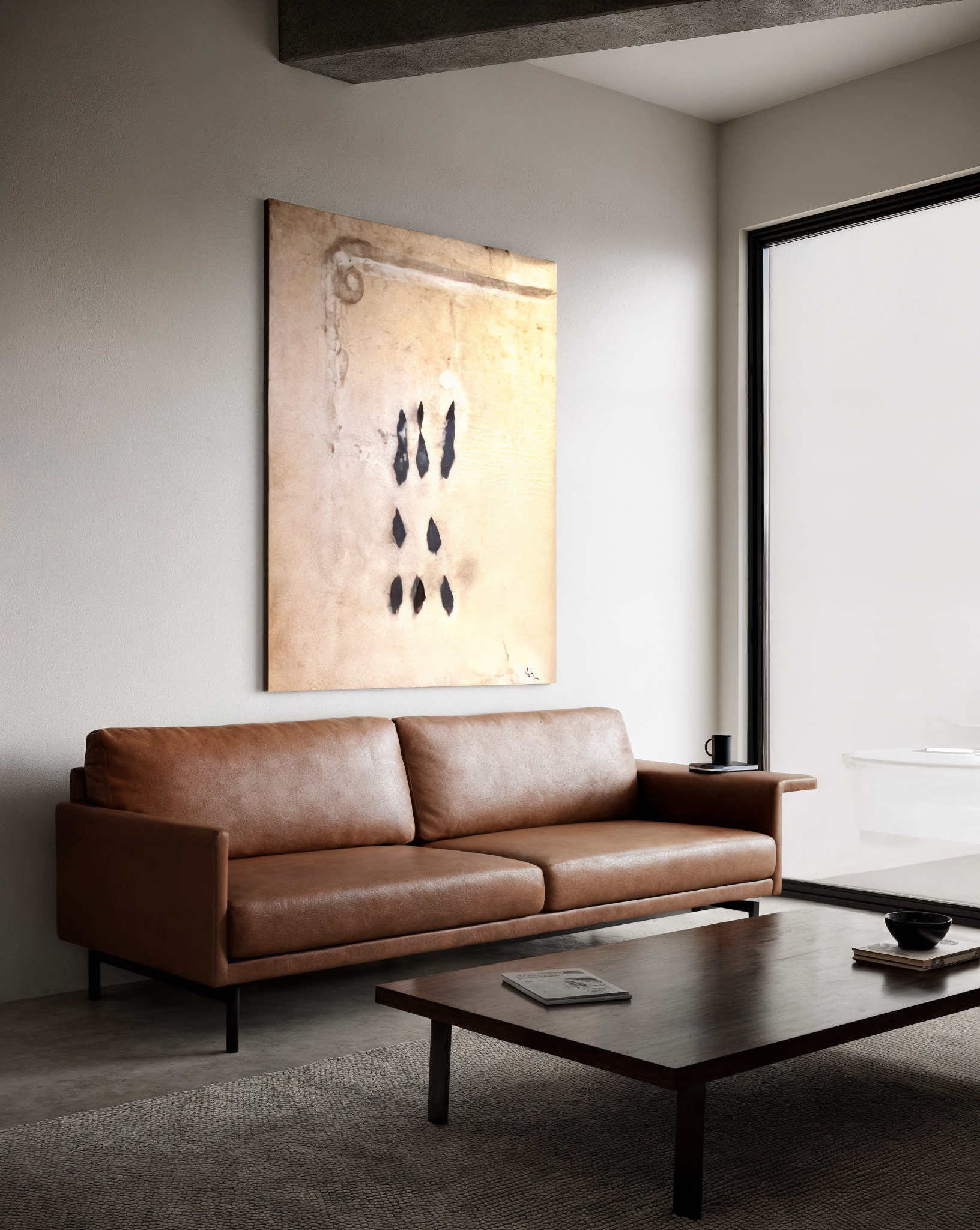 Modern living room with a brown leather sofa, a wooden coffee table, abstract artwork on the wall, and a large window with sliding glass doors.
