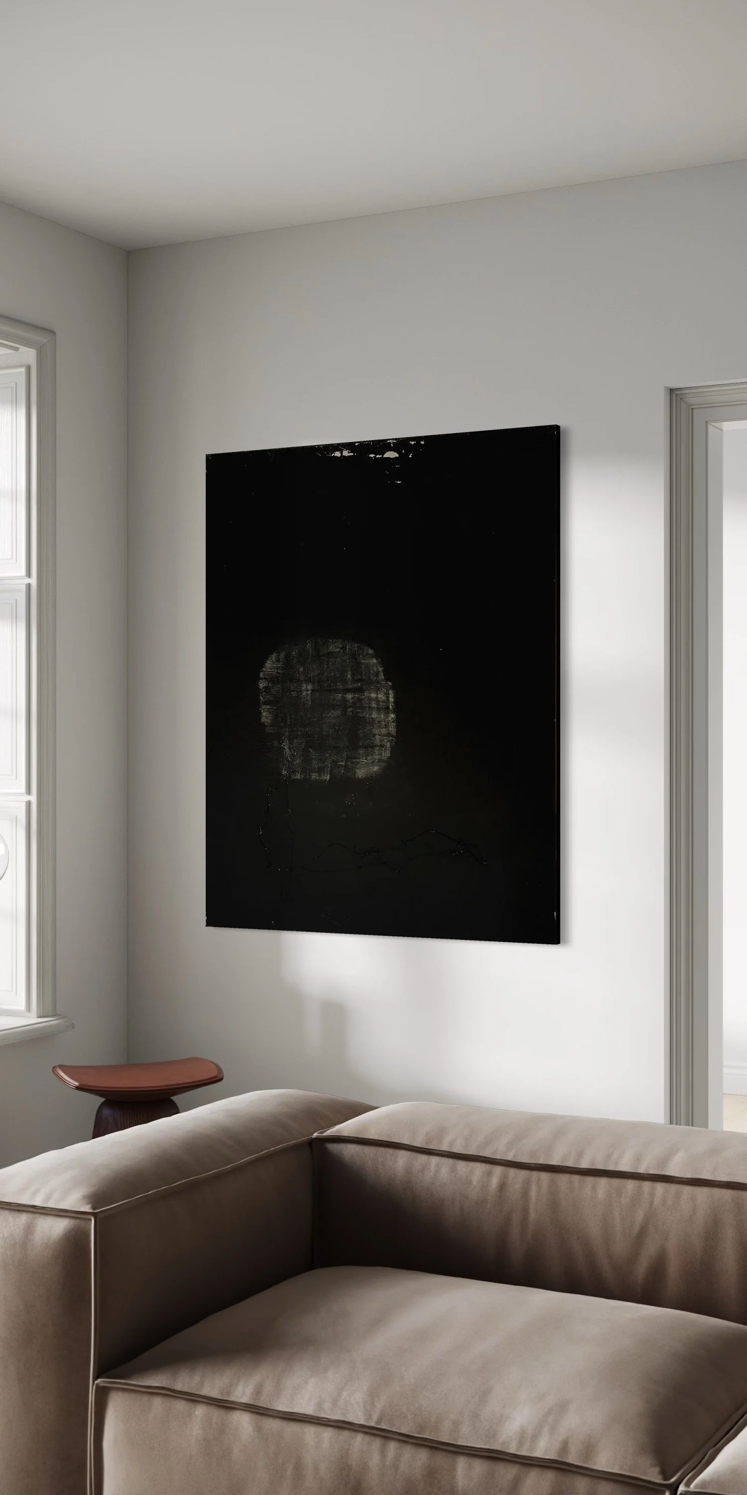 A living room with a white wall, a window, a beige sectional sofa, an art piece on the wall, and a small wooden side table with a curved top.