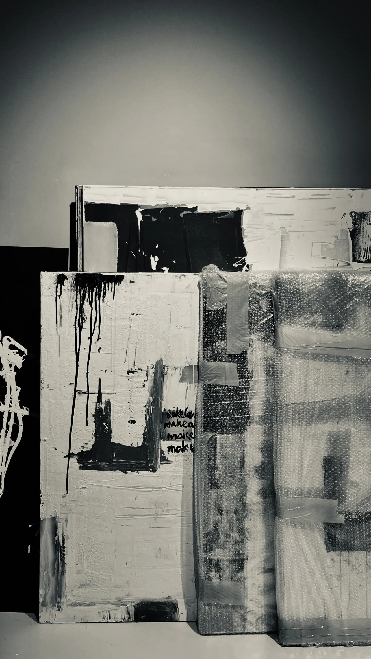 Several abstract, monochrome art canvases stacked against a wall, some with paint drips and textured surfaces.