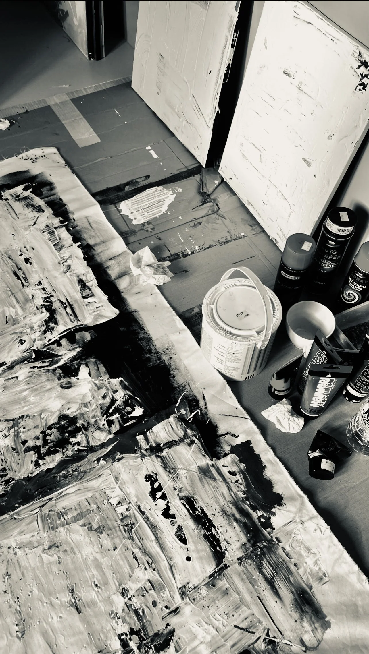 An art studio workspace with abstract black and white paintings, paint supplies, and bottles on a table.