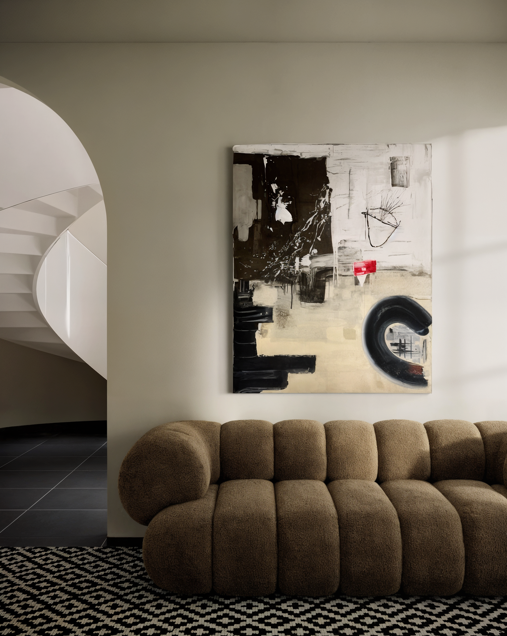 Interior of a modern living room with a beige plush sofa and abstract painting on white wall, with a black and white patterned rug on dark tiled floor.