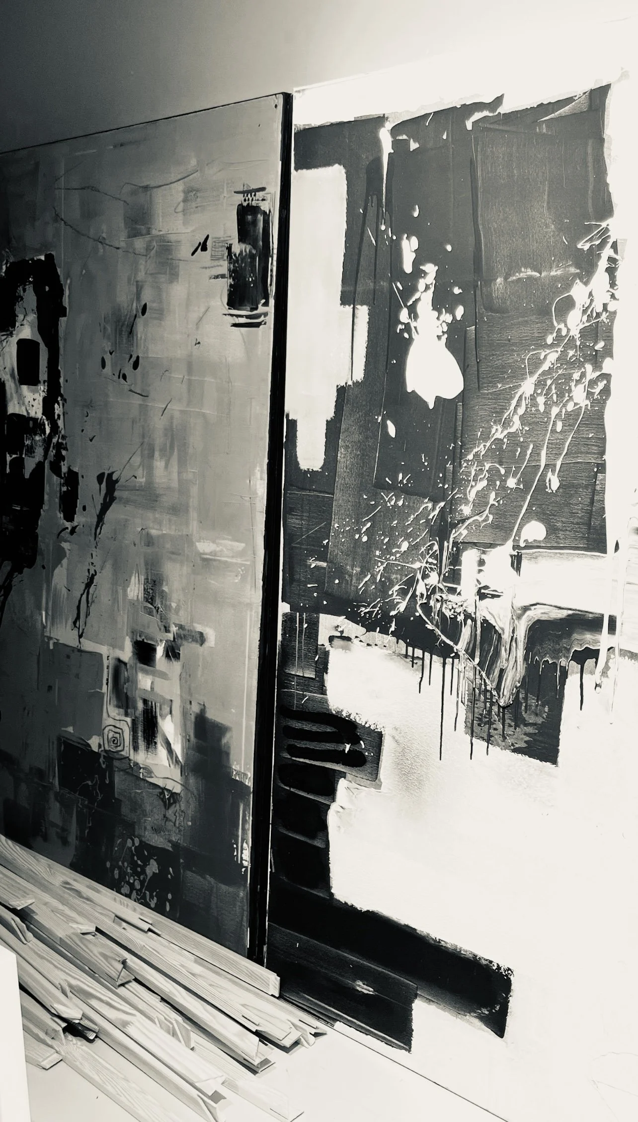 Black and white abstract painting with geometric shapes, paint splatters, and textured layers on a wall, with some construction materials visible in the foreground.