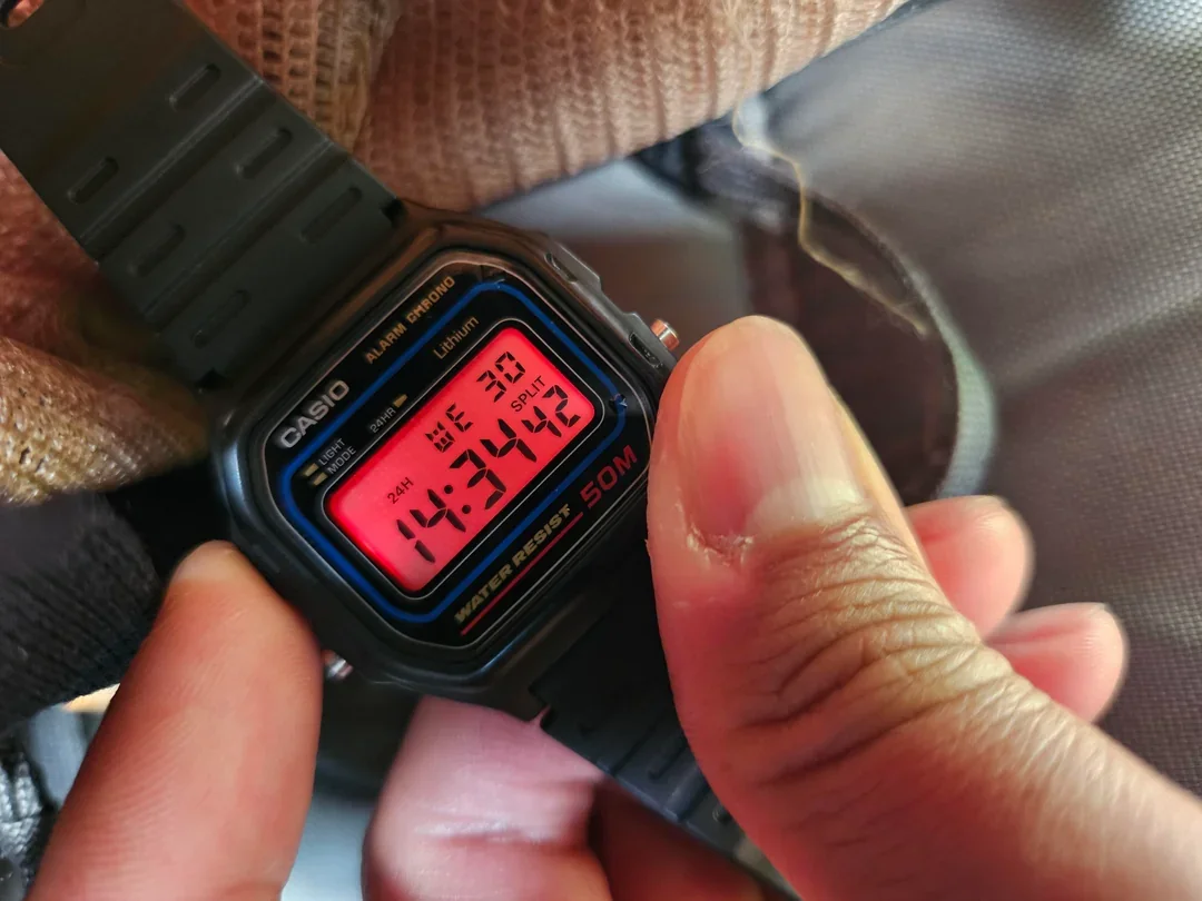 A digital Casio watch showing the date and time of 14:34:42 on December 30, with a red display and black strap.