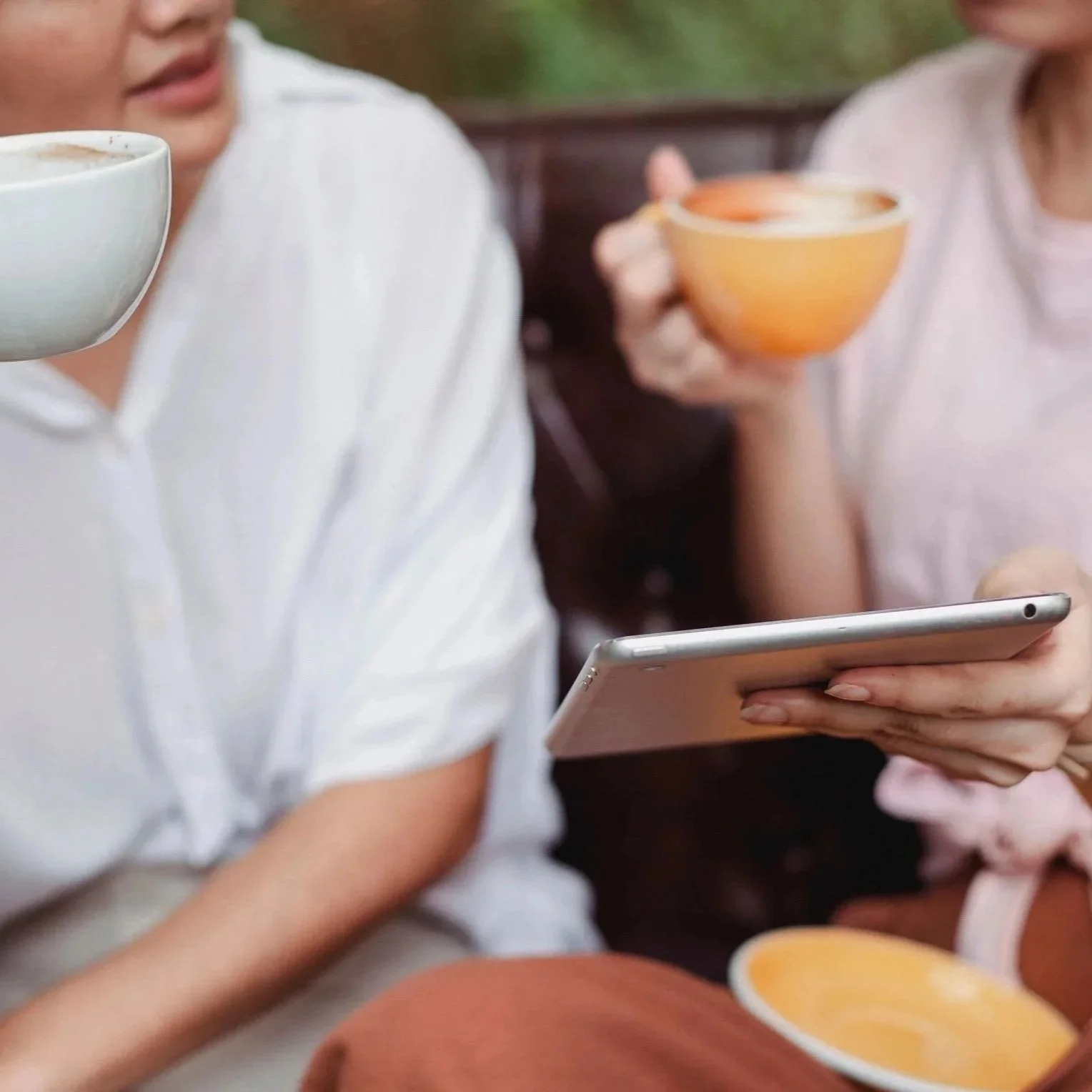 Two people sitting together, one holding a smartphone, the other holding a coffee cup, with a bowl of soup on the table.