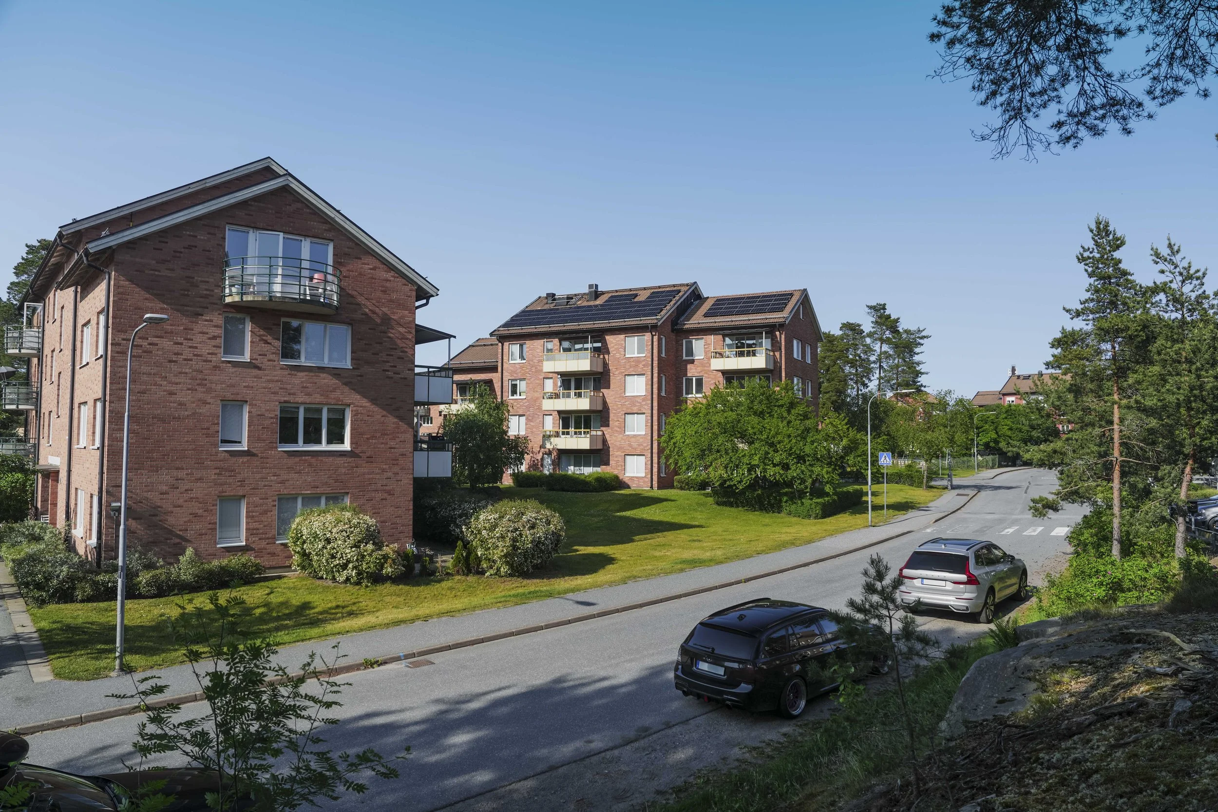 Bostadshus i ett grönt område med parkerade bilar, trevlig dag med klar blå himmel.