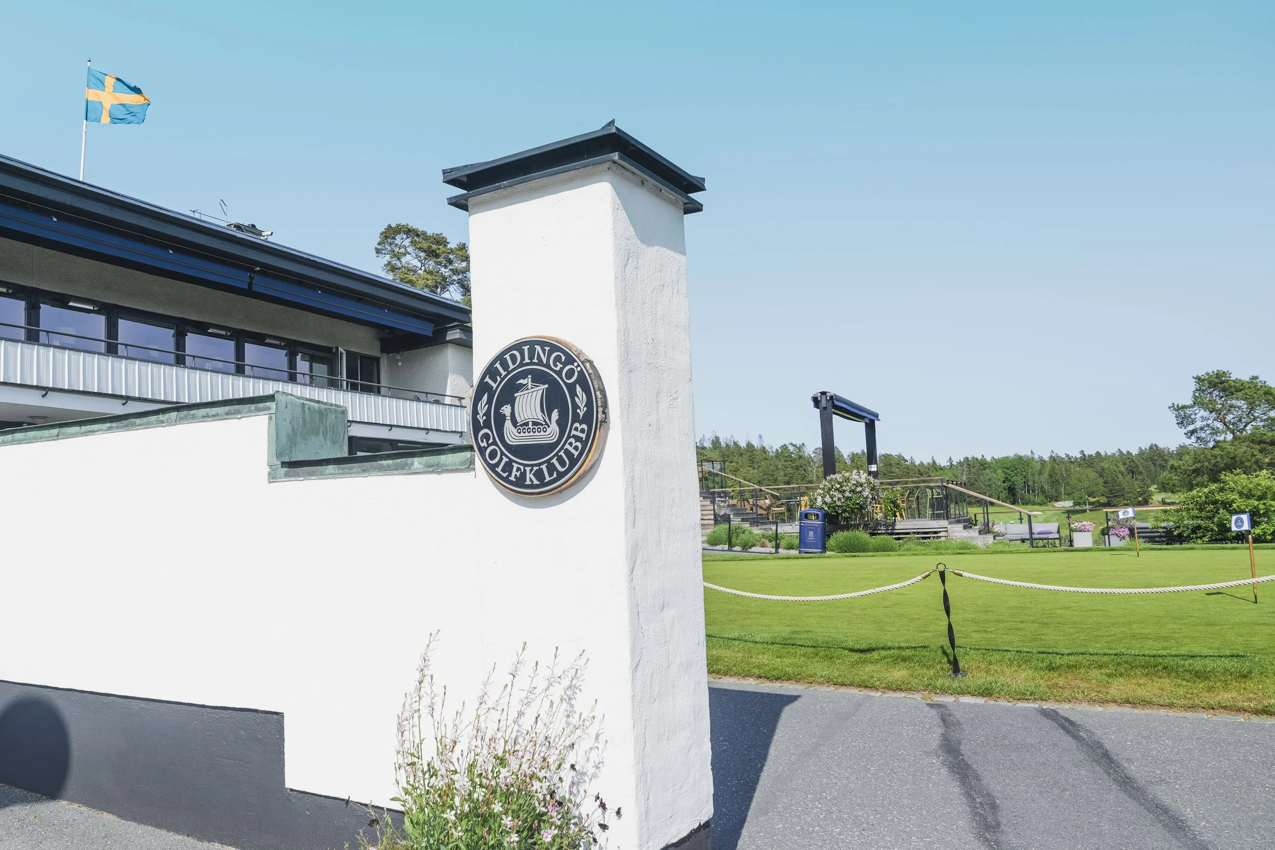 Utsikt av Lidingö Golfklubb med tydlig skylt, grön golfbana och blå himmel.