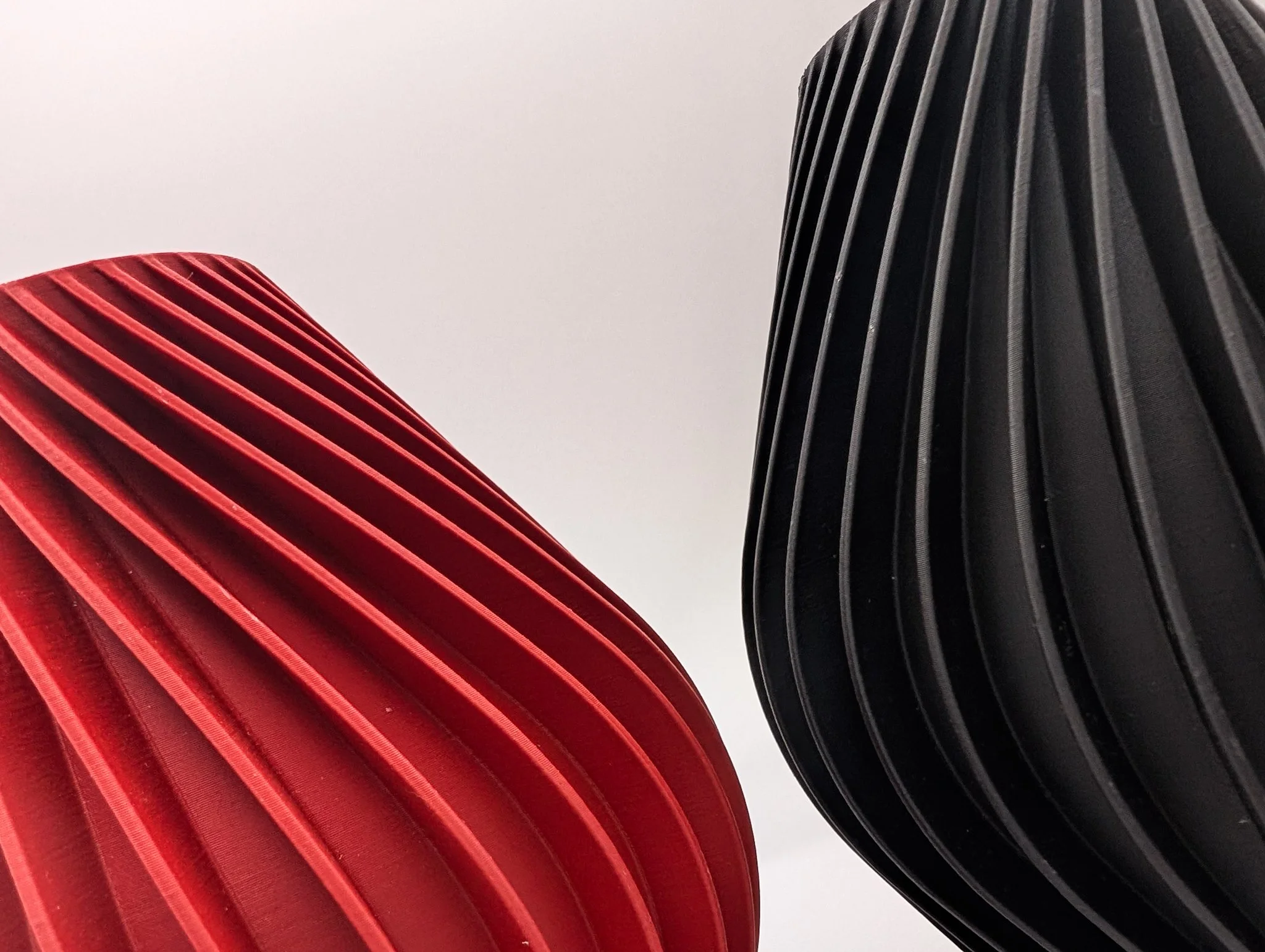 Close-up van twee moderne stoelen, een rode en een zwarte, met gestileerde, spiraalvormige ruggen, gecombineerd in een minimalistische setting.