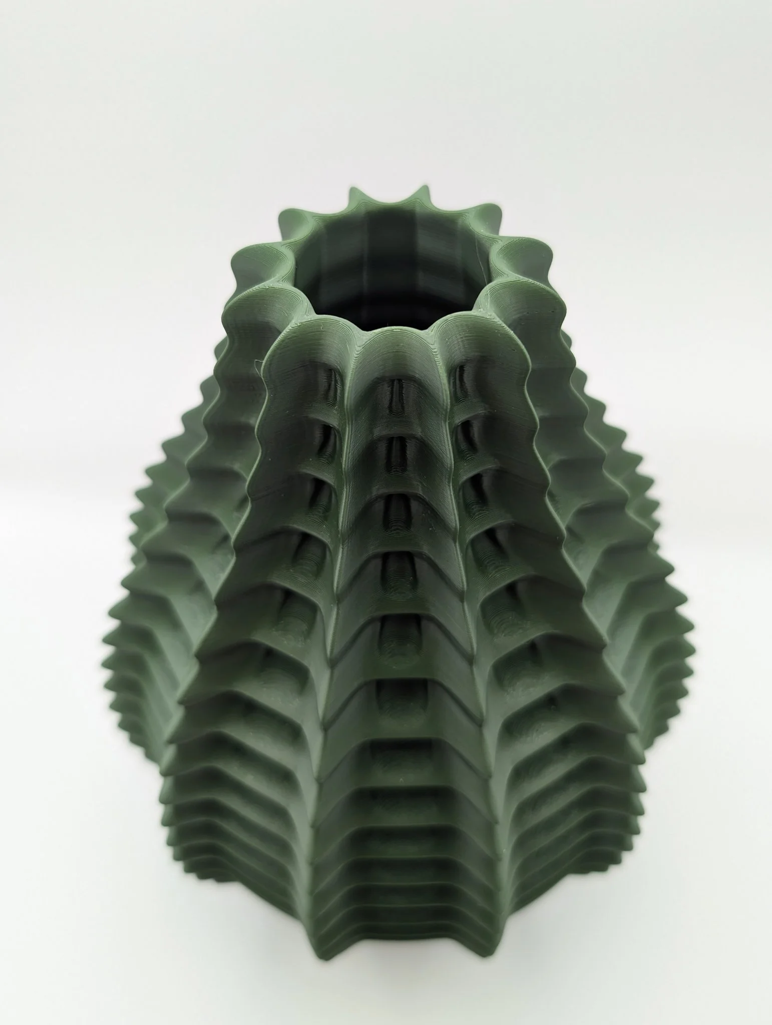 Groene, ribbelige, hedgehog-achtige keramische vaas met een holle opening aan de bovenkant, geplaatst op een witte achtergrond.