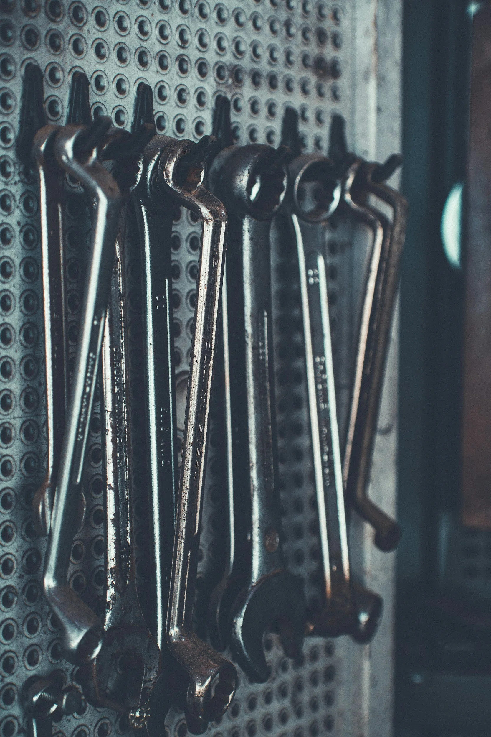 A row of rusty wrenches hanging on a metal pegboard.