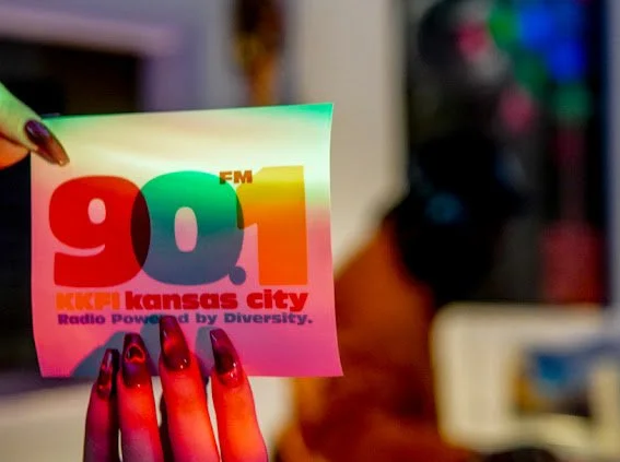 Hand holding a colorful sticker with the radio station 90.1 FM KCKU Kansas City, and the tagline 'Radio Powered by Diversity.'