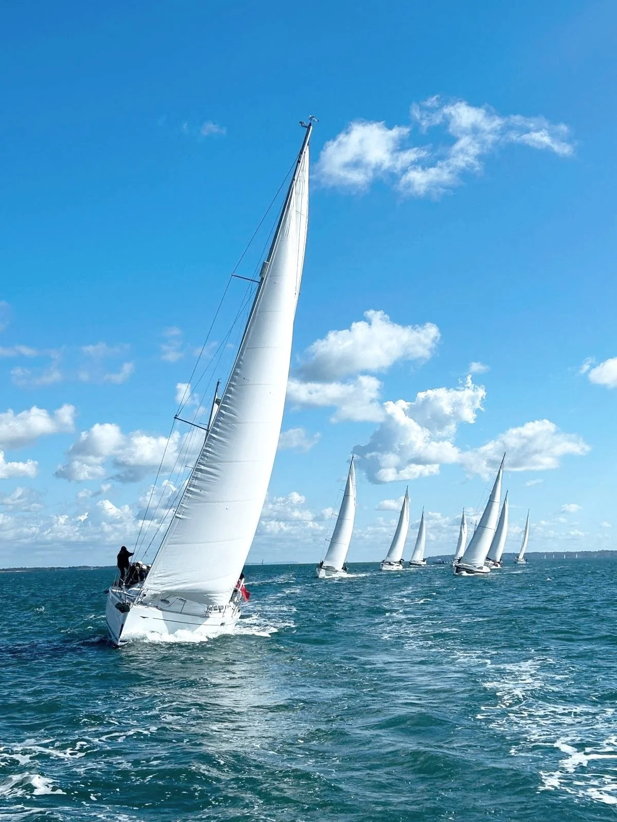 Sailboats racing on the ocean under a blue sky with clouds.