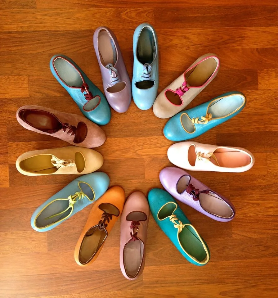 Colorful flamenco shoes arranged in a circle on a wooden floor.