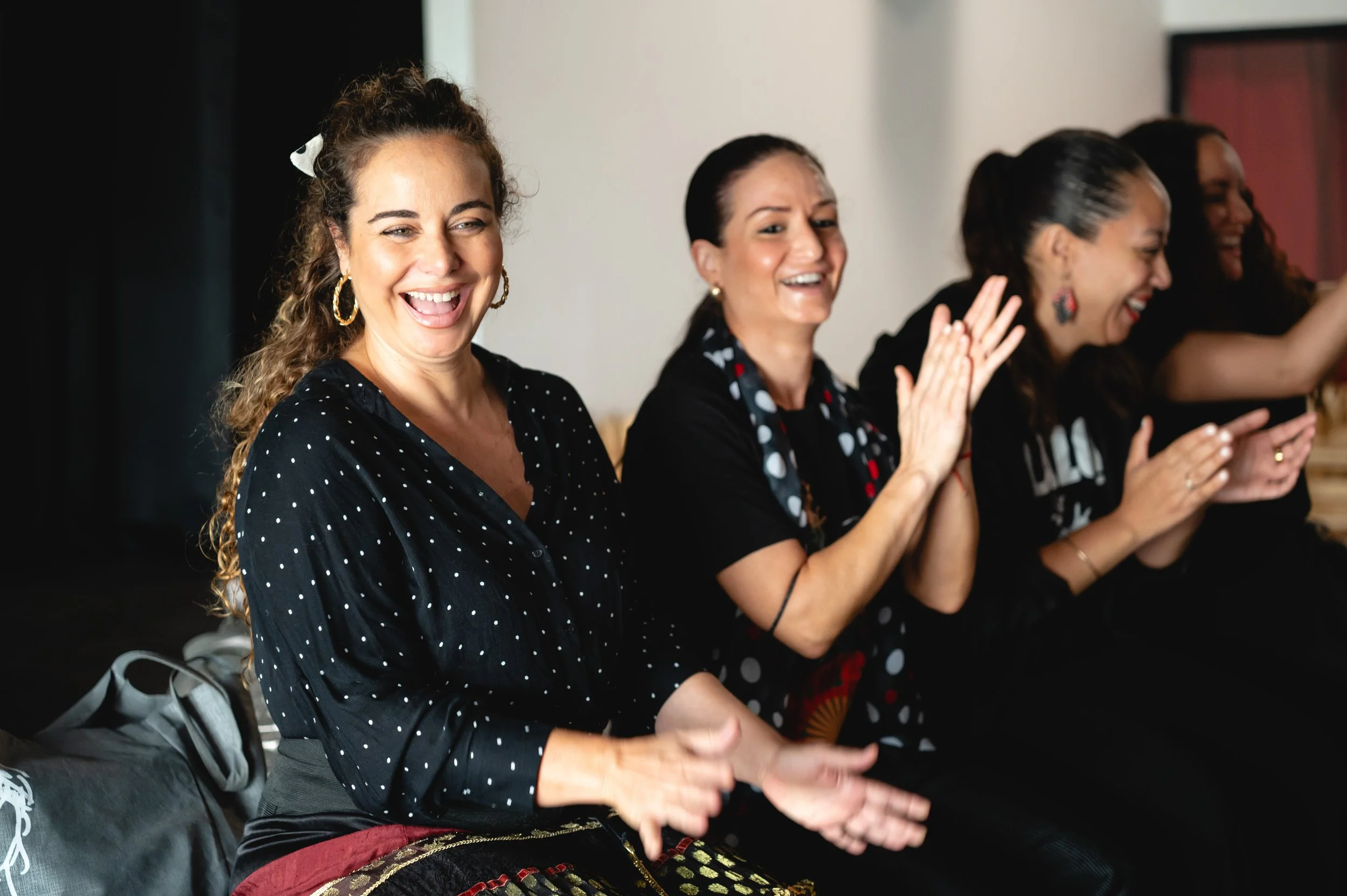Group of women sitting and applauding, smiling and laughing at an indoor event.