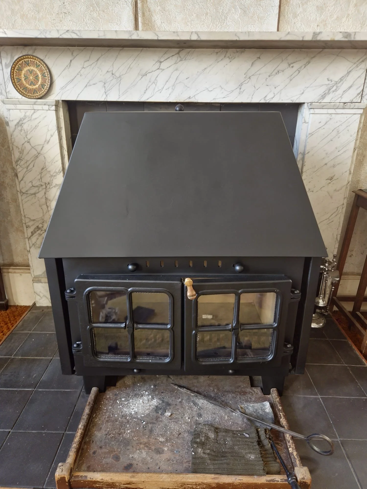 A black cast iron wood-burning stove in a room with tiled flooring and a marble fireplace surround.