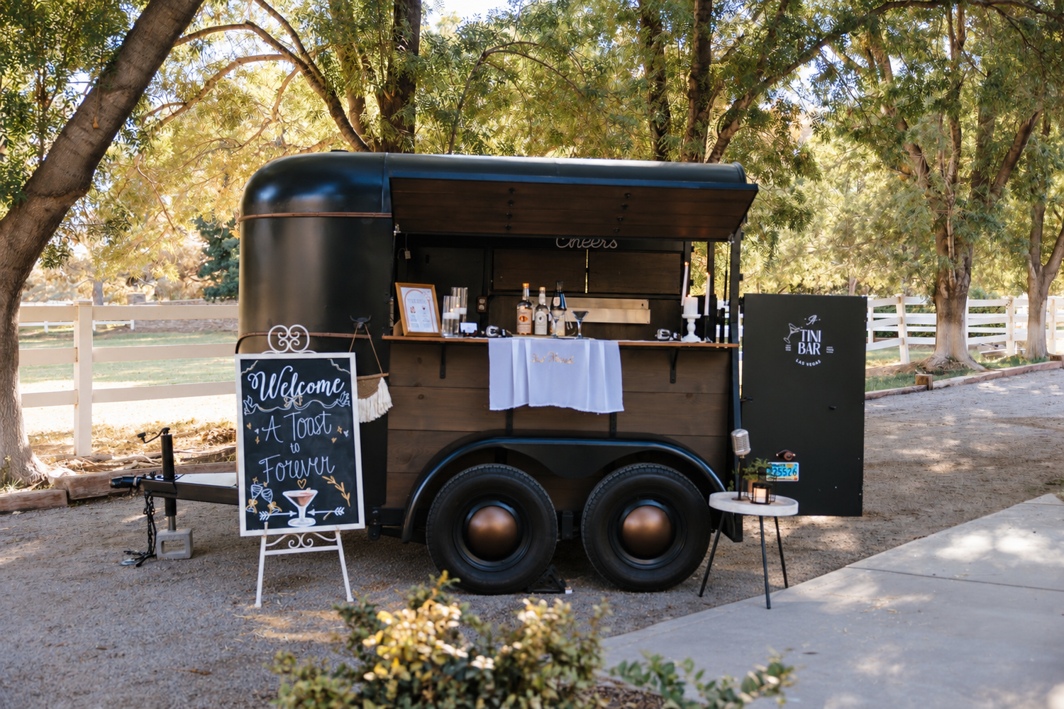 A Tini Bar's vintage horse trailer bar with a Welcome, A Toast to Forever chalkboard sign at a ranch wedding