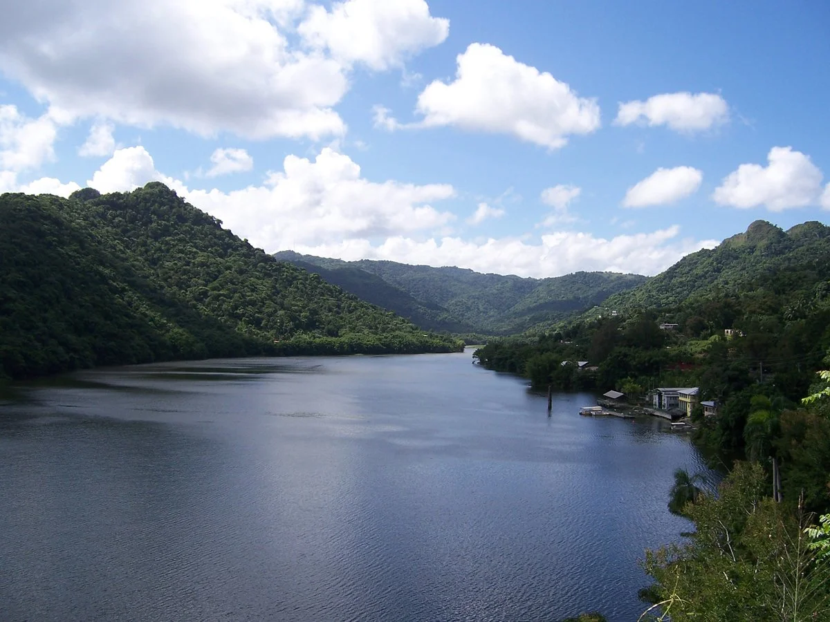 A river flowing between green hills under a partly cloudy blue sky.