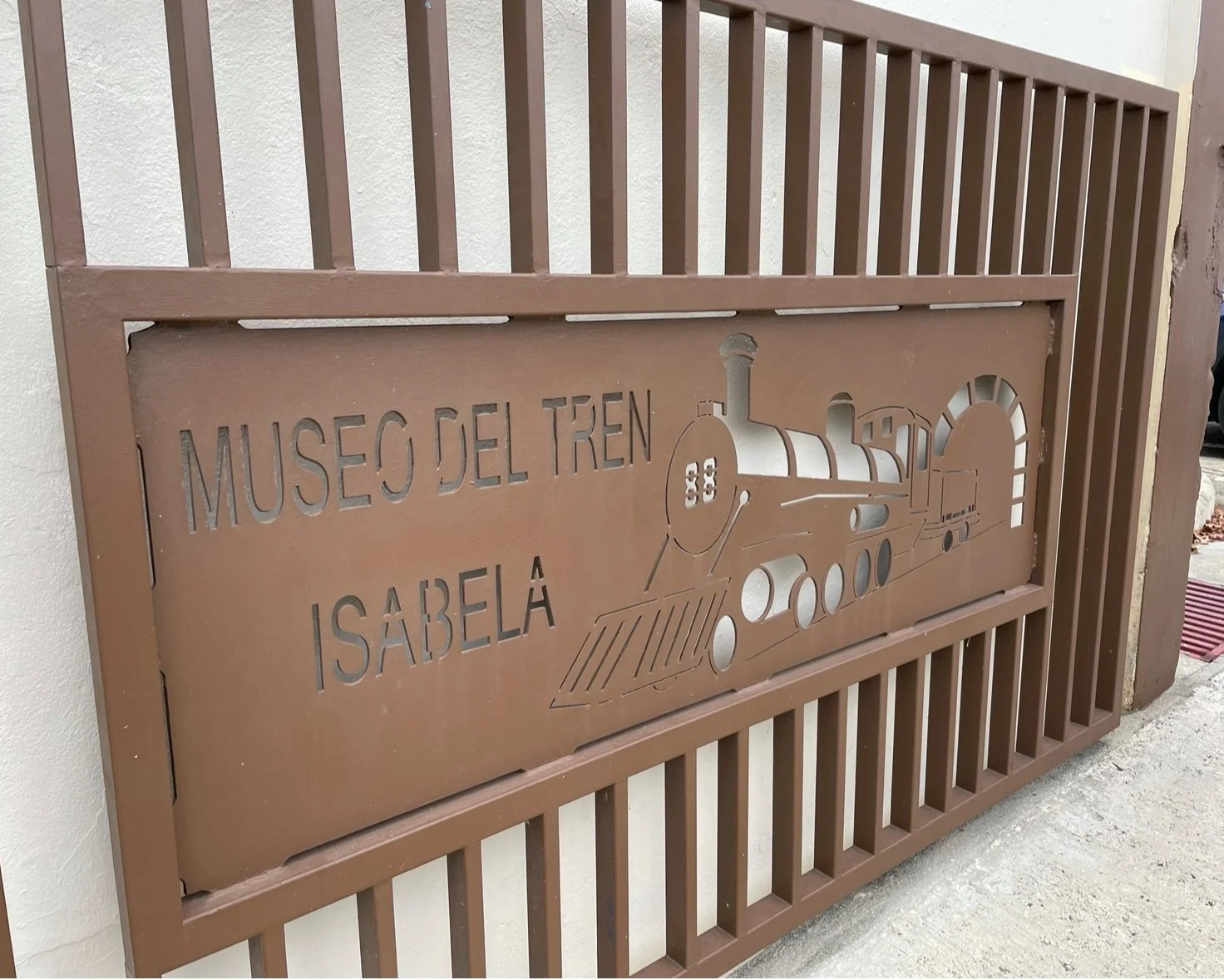 Metal sign with cut-out text and train illustration that reads "Museo del Tren Isabela". by Melanie Mercado
