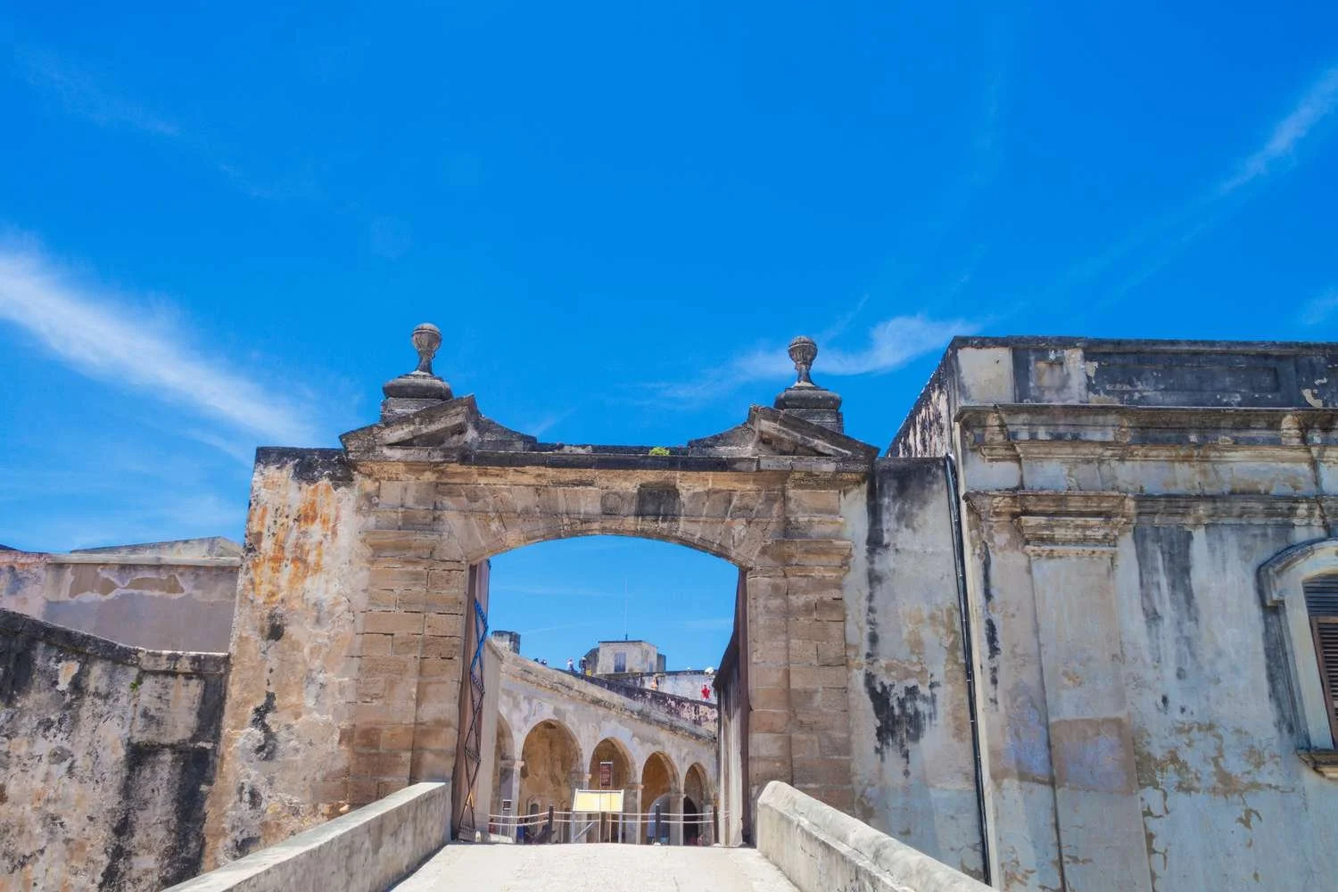 Historic stone archway and walls under a bright blue sky, part of an old fortress or building in a historic site.