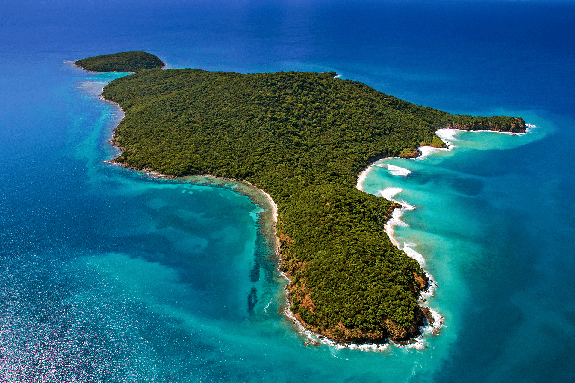 Aerial view of a lush green island surrounded by turquoise waters with white sandy beaches.