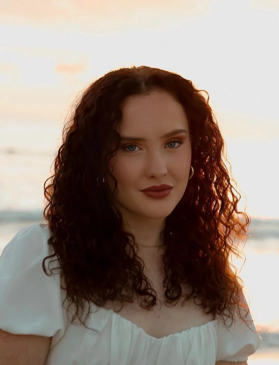 Woman with curly hair and white dress at sunset on beach
