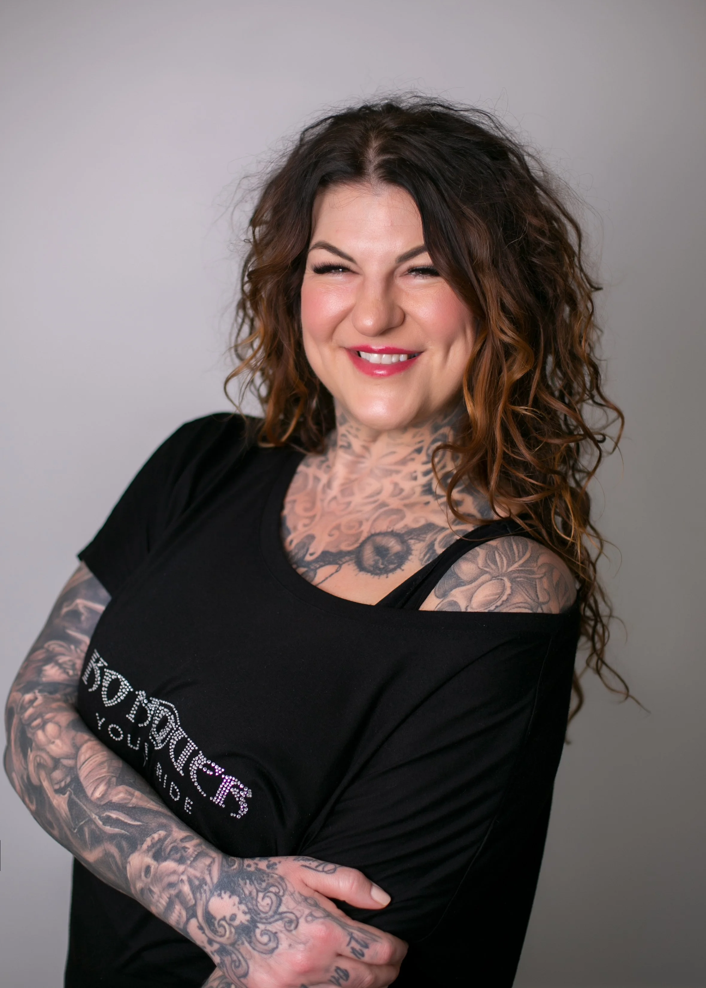 Smiling tattooed woman with curly brown hair wearing a black top
