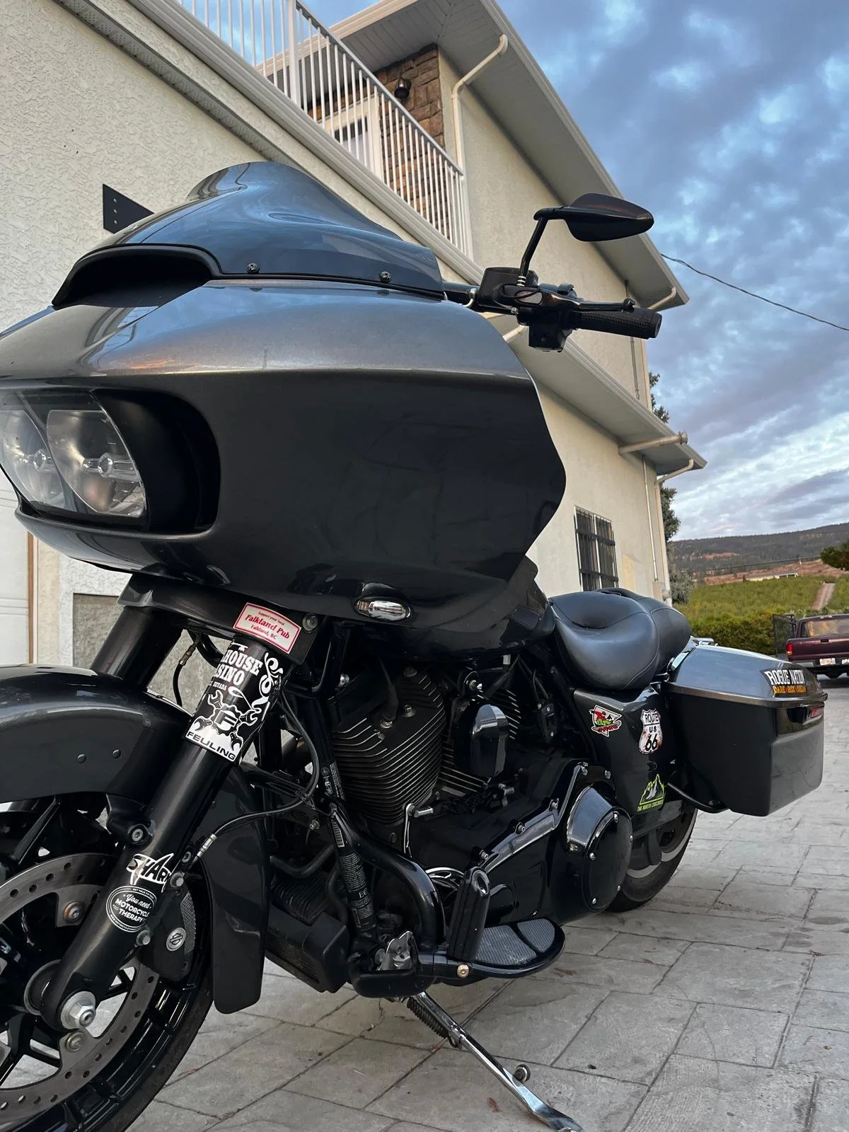Black touring motorcycle with windshield, saddlebags, chrome engine, and stickers parked beside a house.