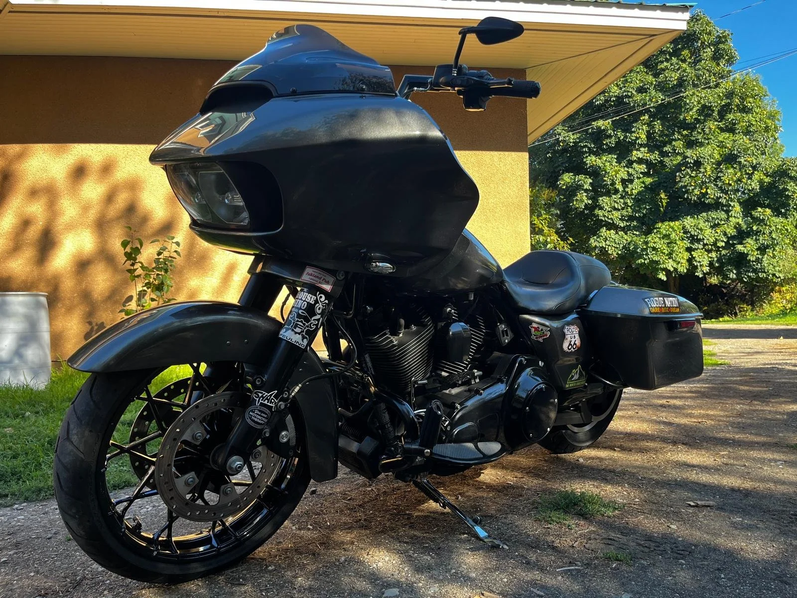 Black touring motorcycle with front fairing, saddlebags, and stickers parked outside a house.