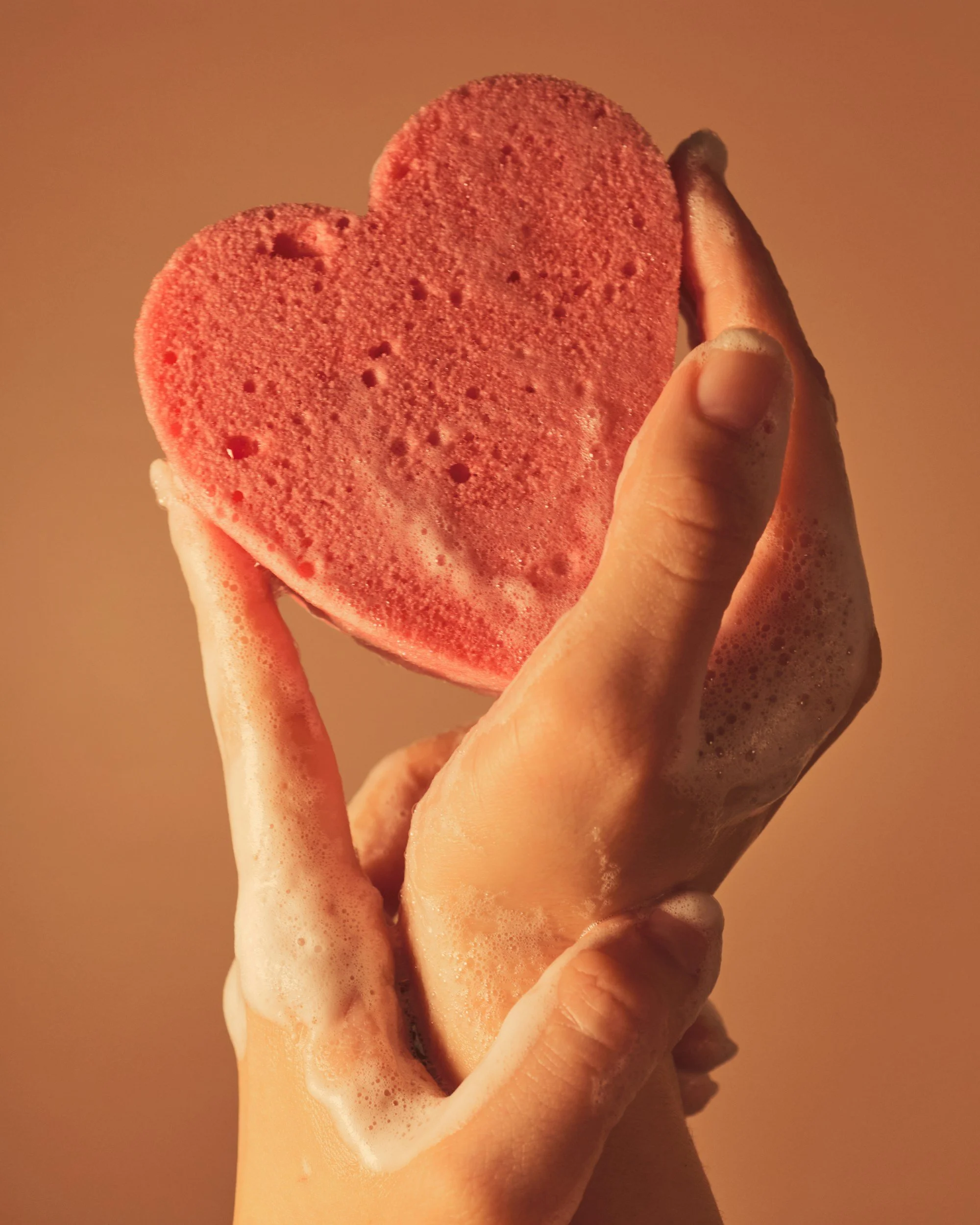 A hand holding a pink heart-shaped bath bomb with bubbles on the surface.
