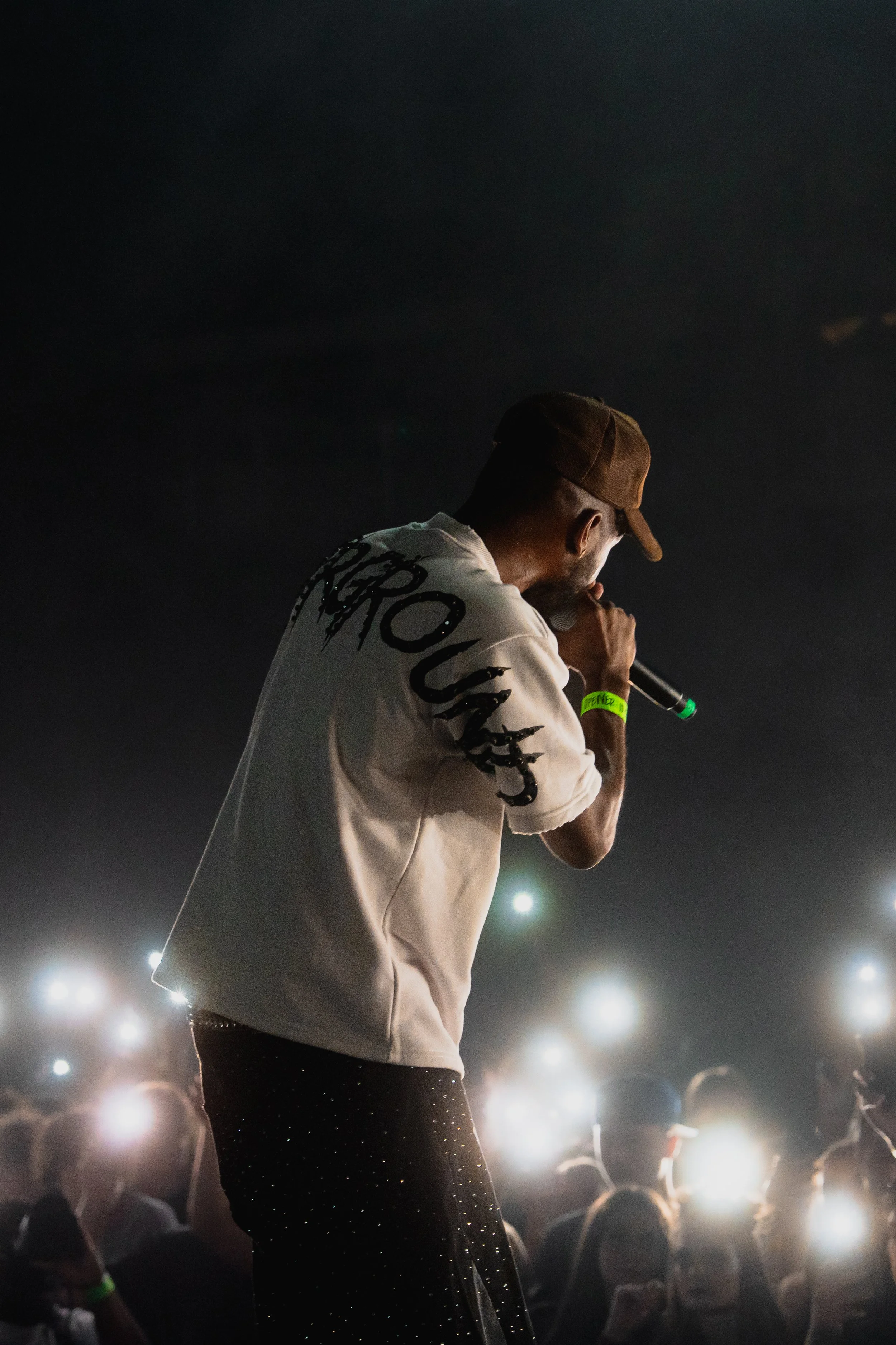 Performer singing into a microphone on stage at night with audience members holding up their phones with lights on.