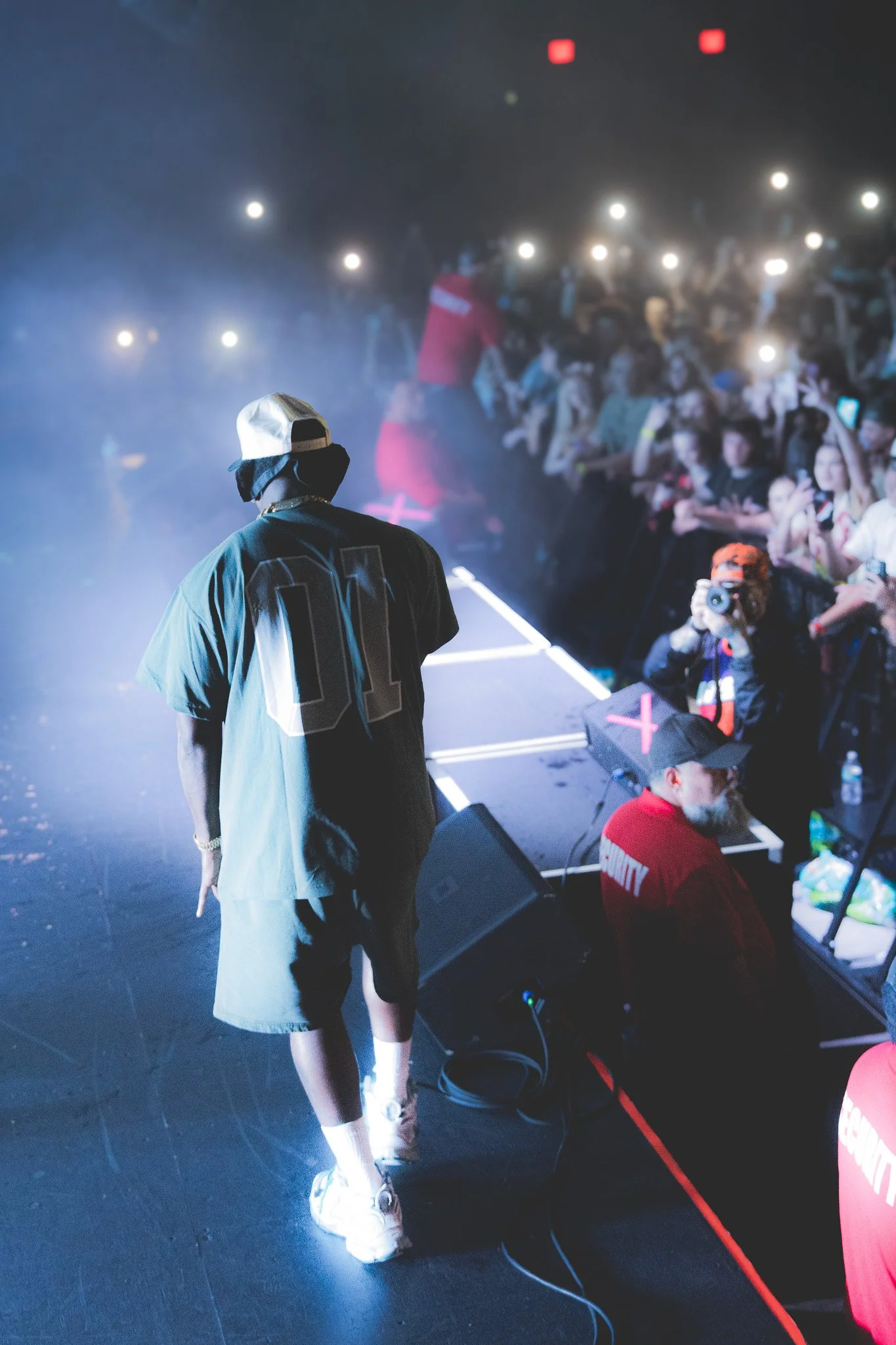 A performer on stage facing an audience with many people holding up phones and taking pictures at a concert or event.