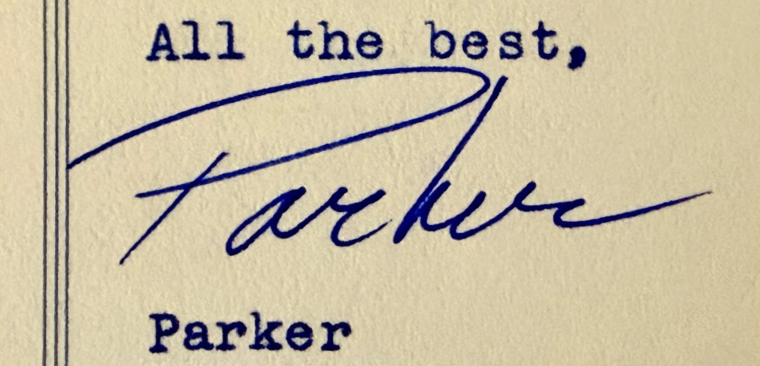 Close-up of a handwritten signature and printed text on an envelope or letter. The signature is cursive, blue ink, and reads 'Jackie'. The printed text includes 'All the best,' and 'Parker'.