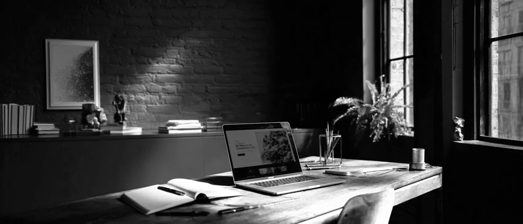 Sunlit loft office with a desk, plants, and tall industrial windows