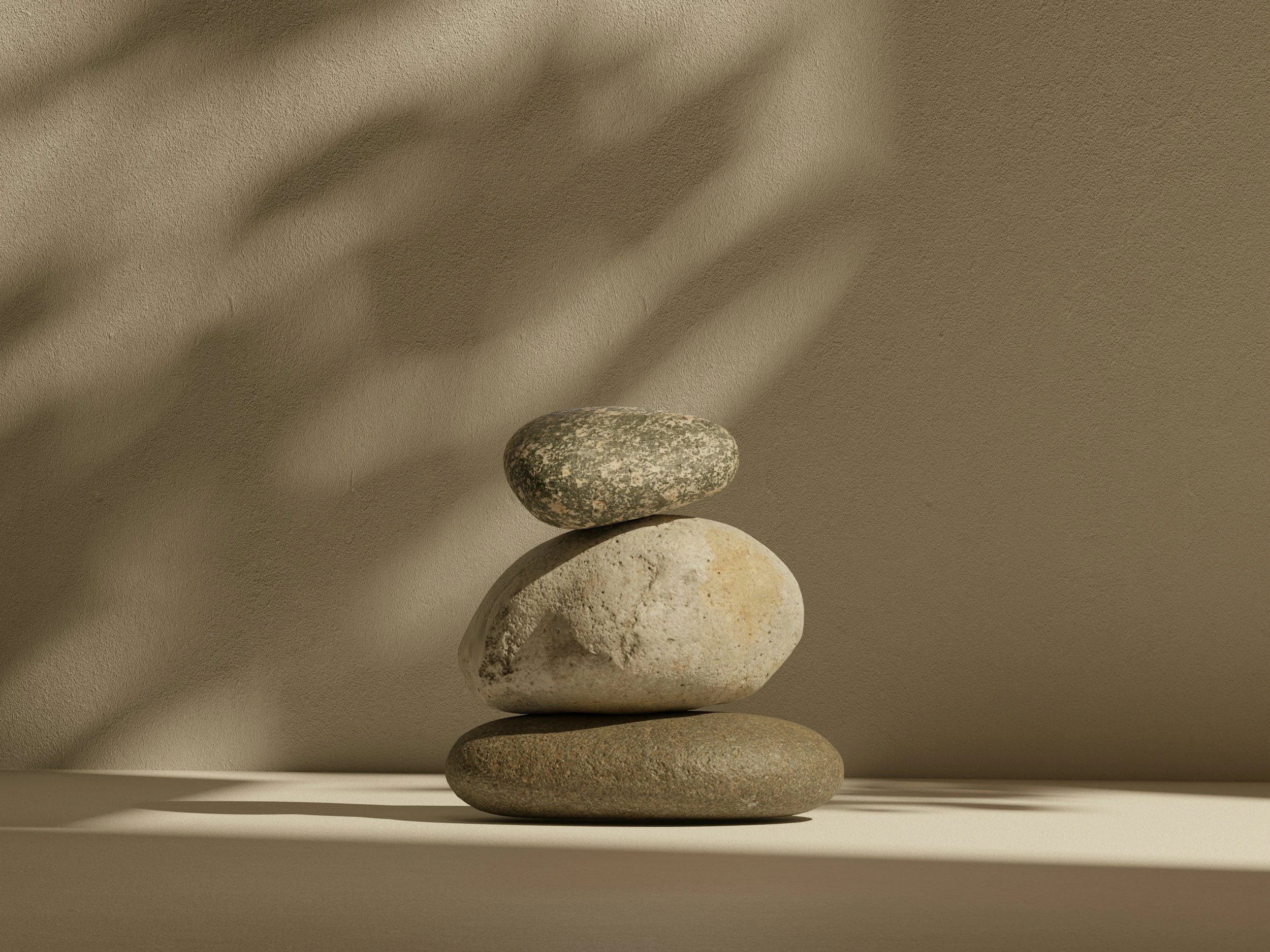 Three stacked stones on a table with a beige background and shadows.