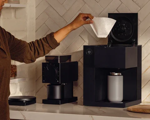 Person pouring coffee into a cup from a coffee machine in a kitchen.