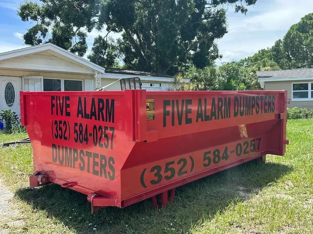 Red 12-yard roll-off dumpster from Five Alarm Dumpsters placed in a residential driveway, representing affordable rental pricing in Hernando, Pasco, and Citrus Counties.