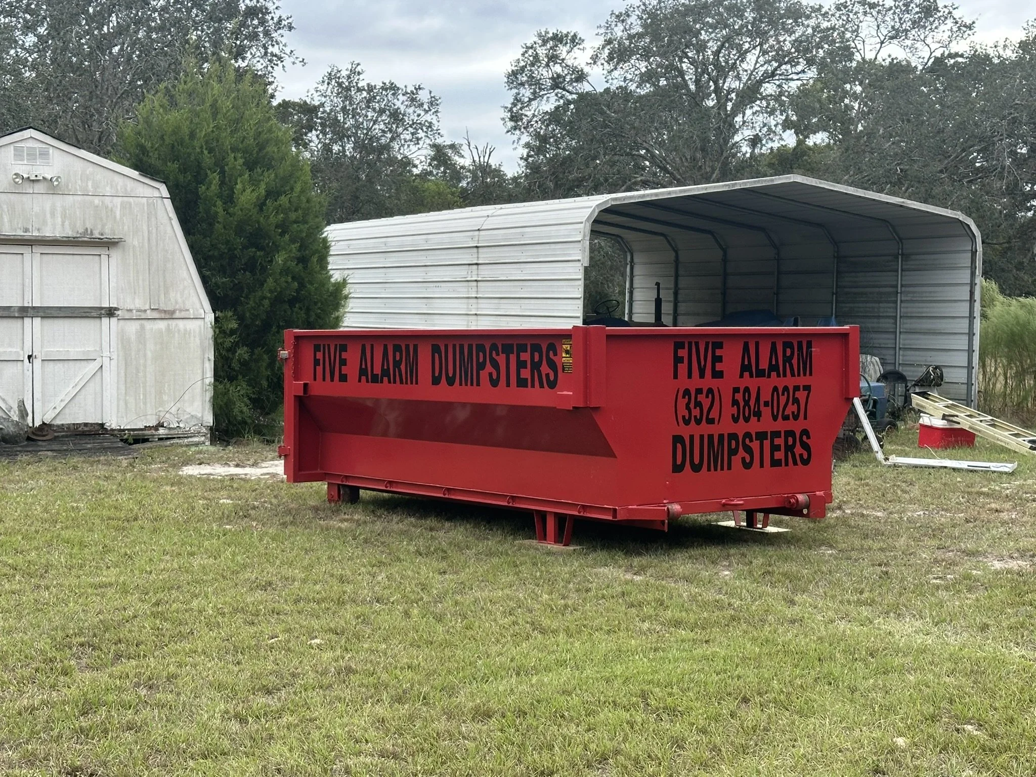 12-yard roll-off dumpster rental placed in front of a shed for a cleanout in Hudson, Florida