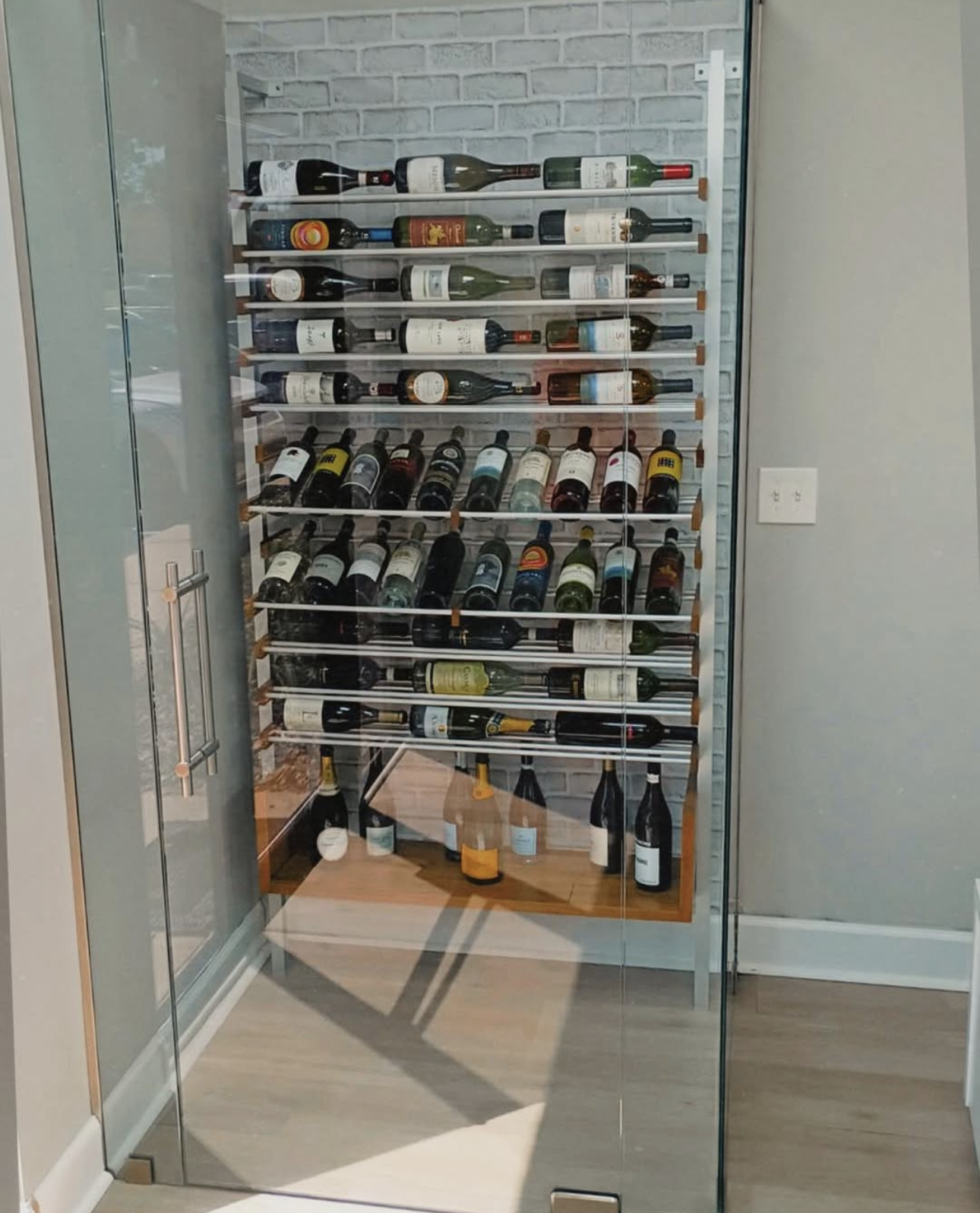 A luxurious wine cellar with wood-paneled walls and ceiling, enclosed by glass doors, with rows of wine bottles on horizontal racks.