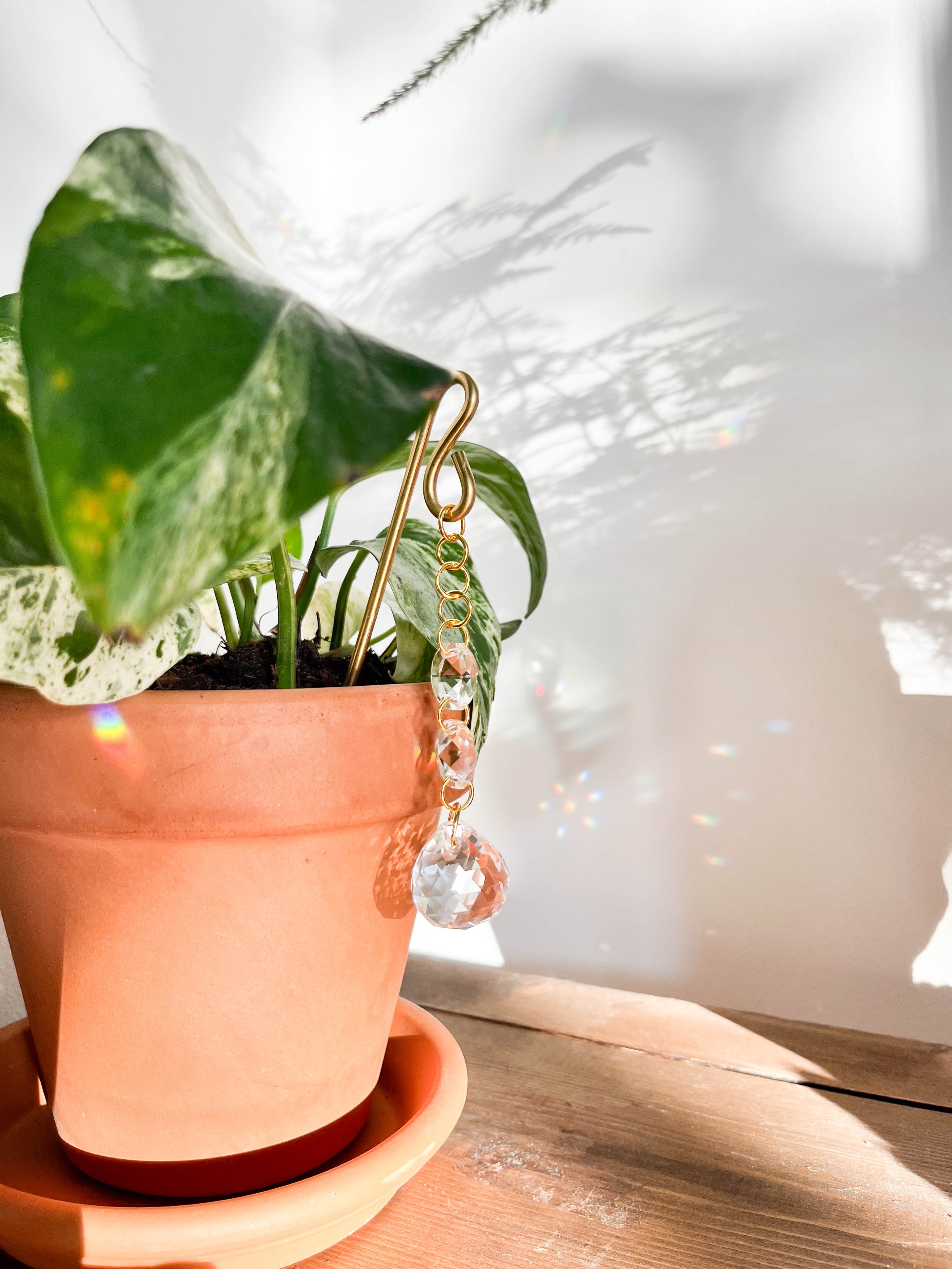 Gold sun catcher with three faceted crystal prisms hanging from a delicate chain, designed to create beautiful rainbow light reflections indoors.