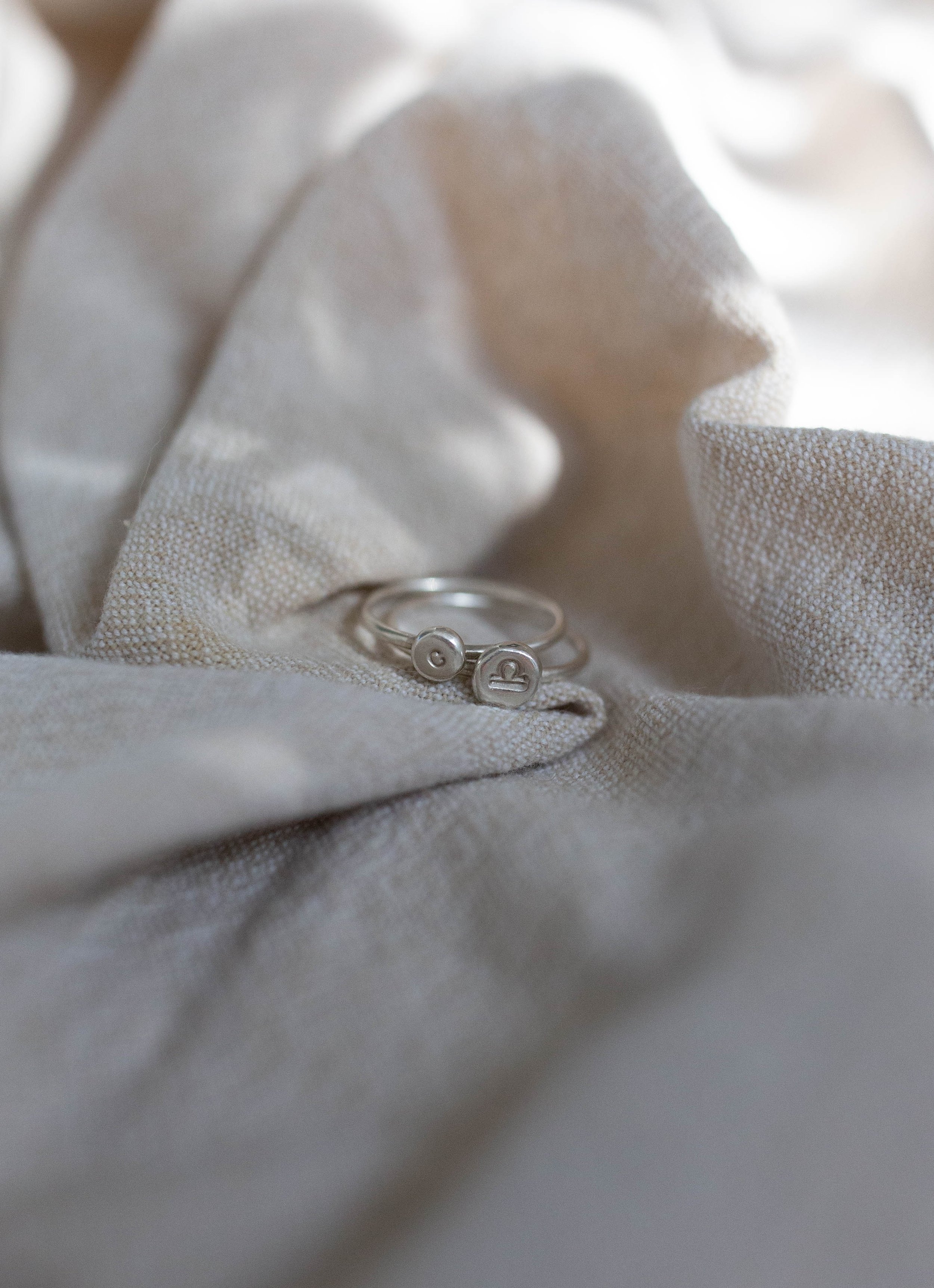 Close-up of two silver stacking rings with initial and star sign tokens on textured fabric