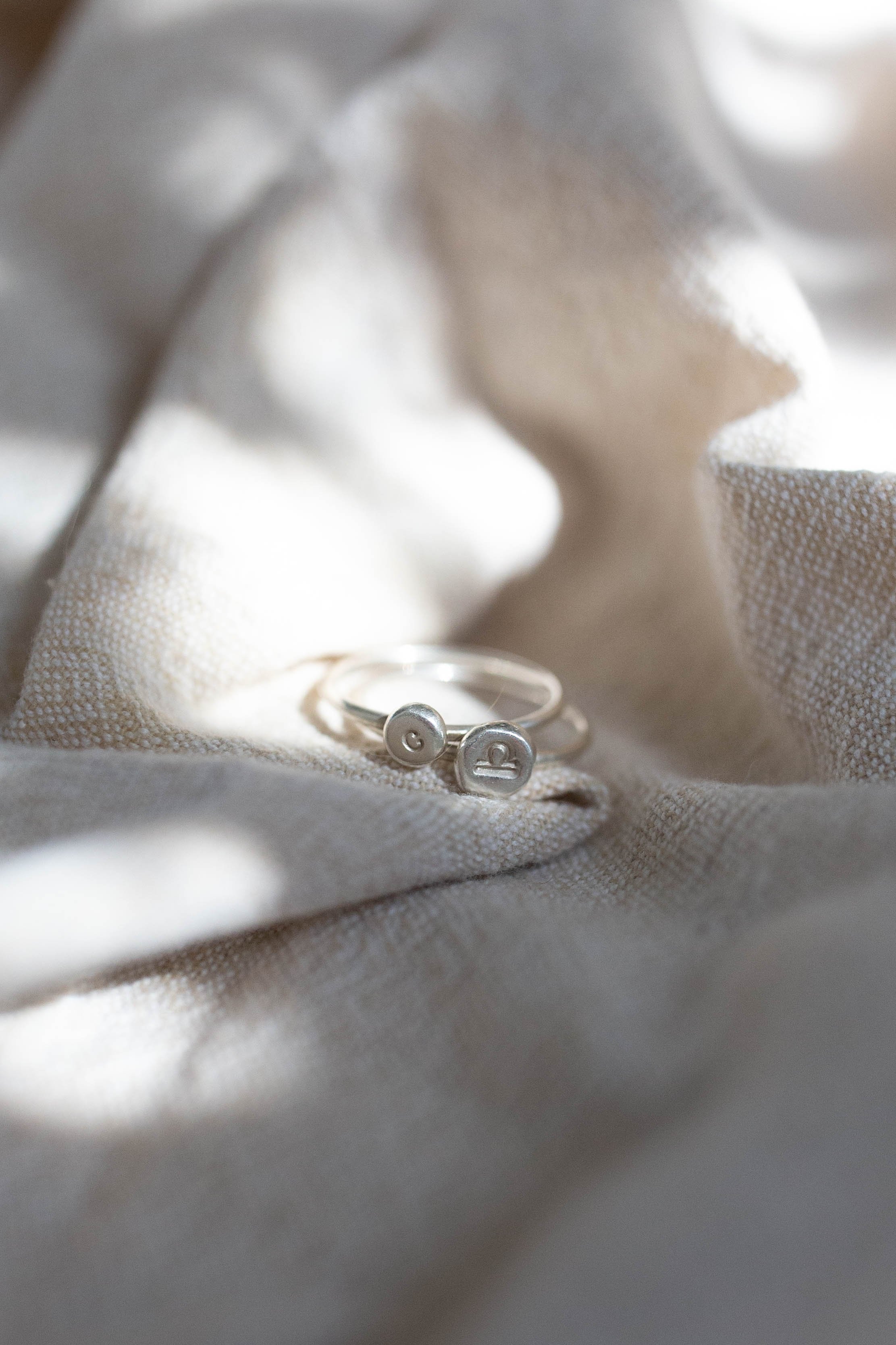 Minimalist silver stacking rings featuring custom initials and zodiac signs under dappled sunlight