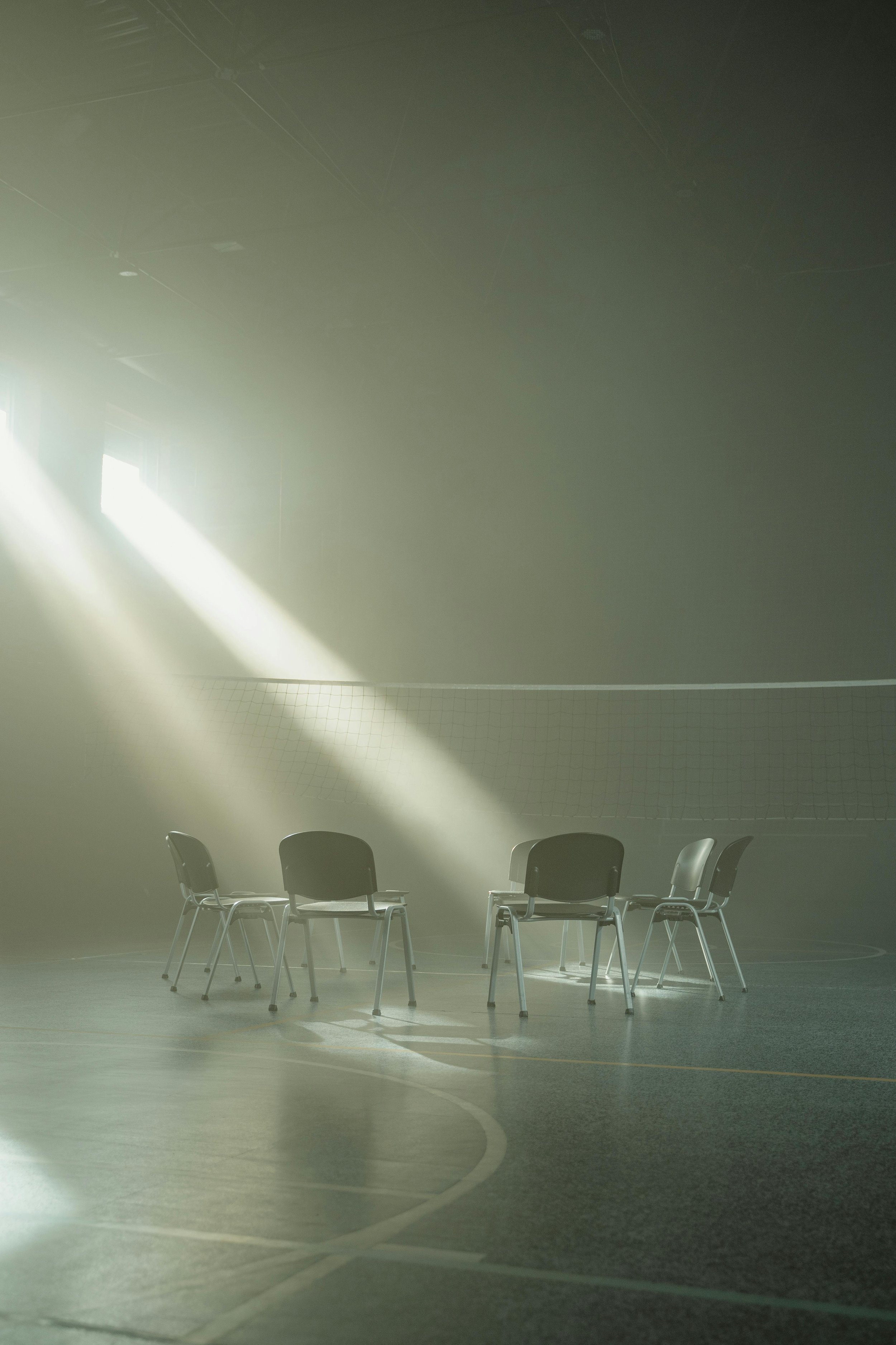 Empty chairs arranged in a circle in a gymnasium with sunlight streaming through the windows.