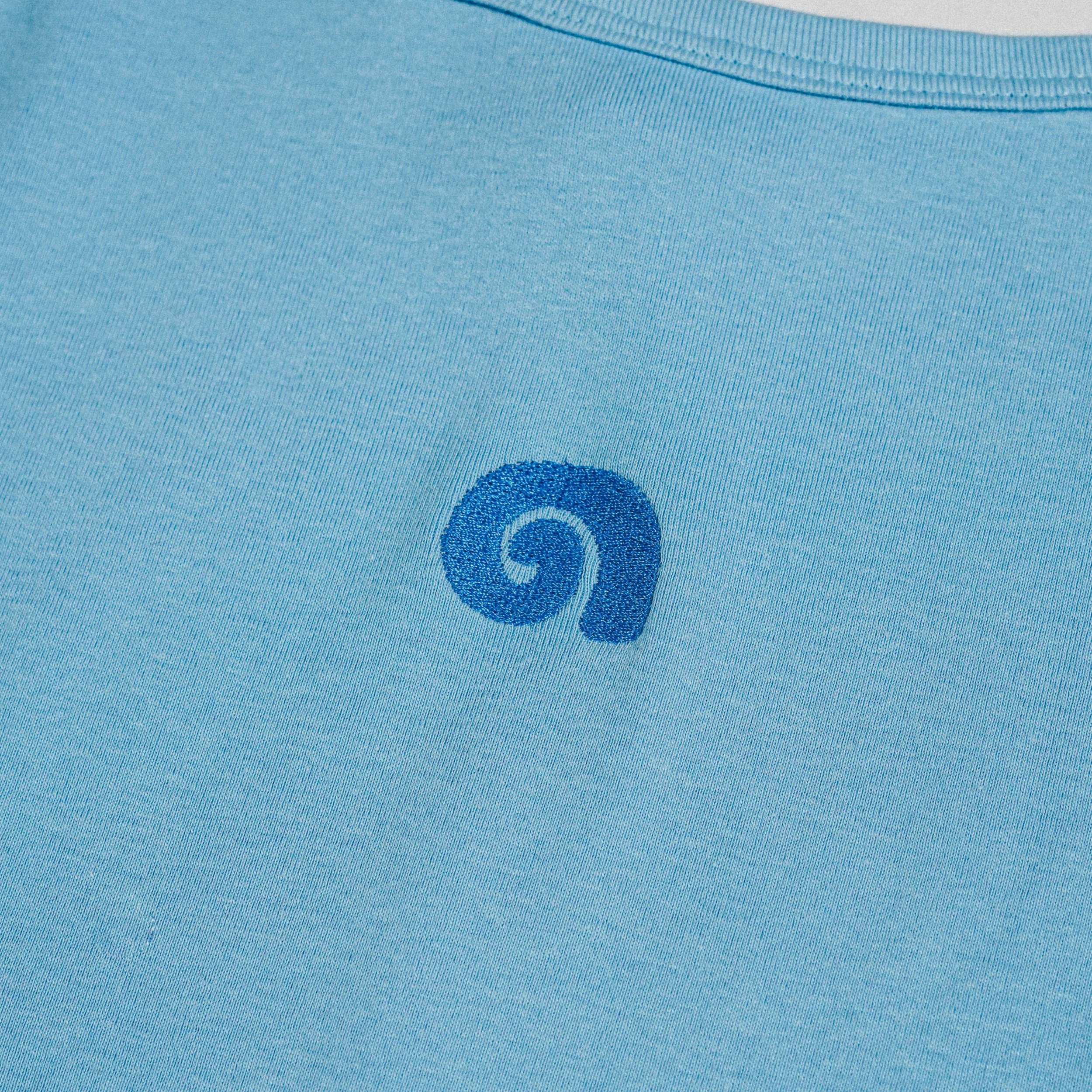 Close-up of a light blue fabric shirt with a small, dark blue embroidered swirl logo.