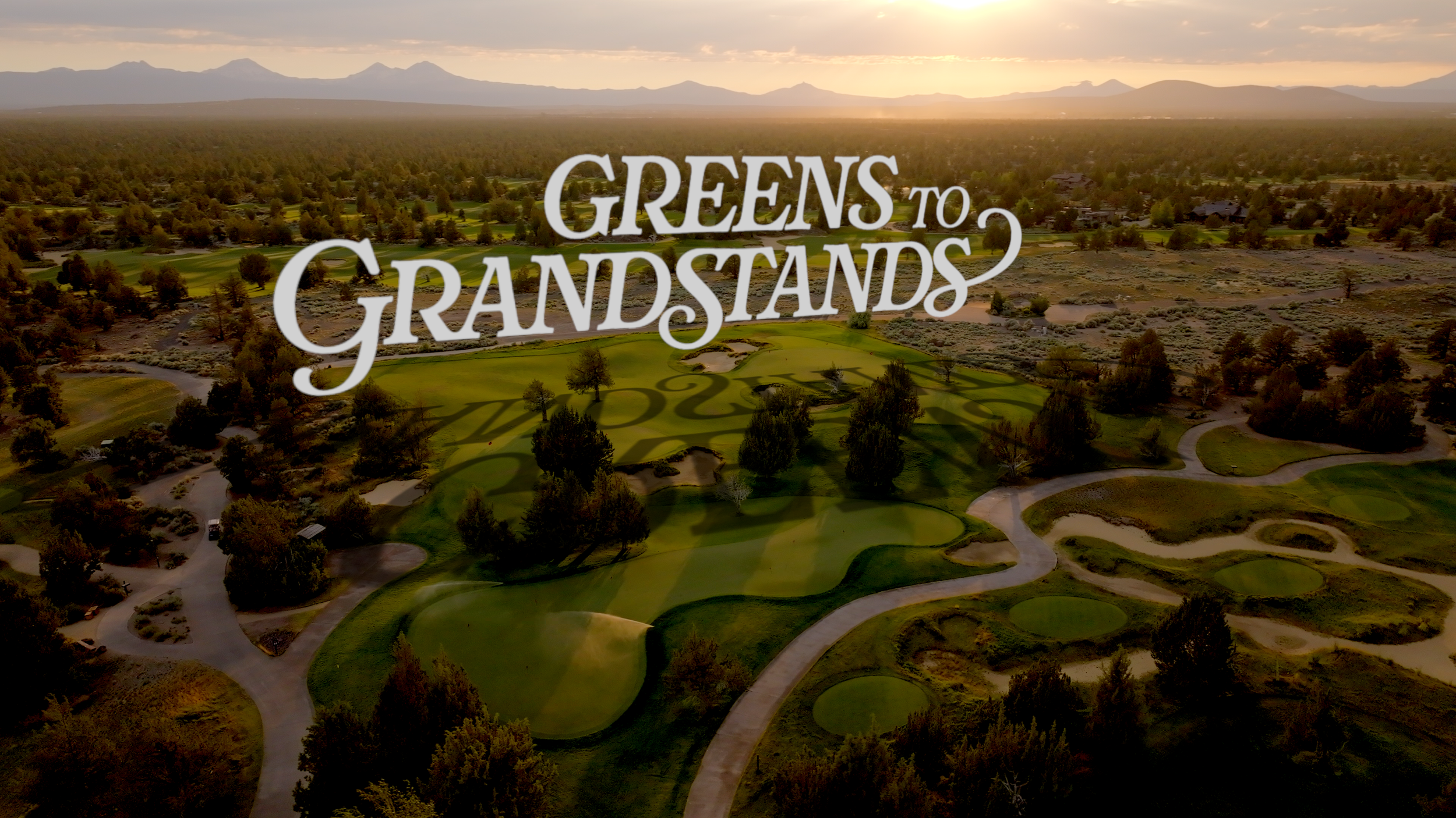 Aerial view of a golf course with fairways, greens, sand traps, and trees at sunset, with mountains in the background and the text 'Greens to Grandstands' overlaid.